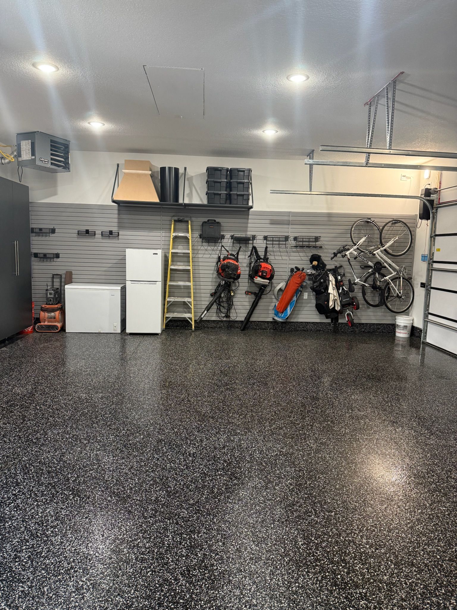 Garage with speckled floor, white walls, shelves, ladder, bicycles, and tools neatly organized.