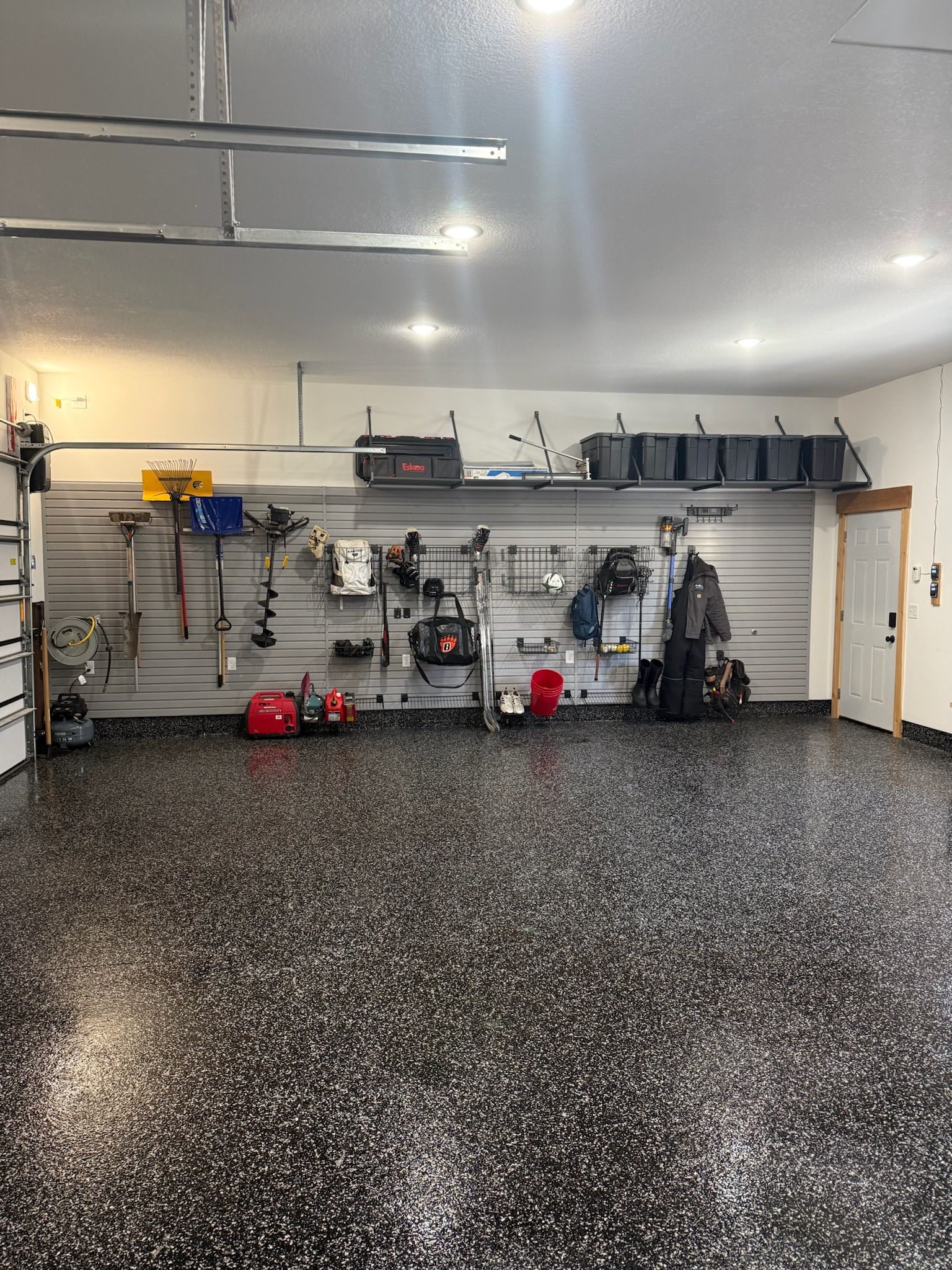 Garage interior with speckled epoxy floor, wall-mounted tools, shelves, and equipment along the back wall