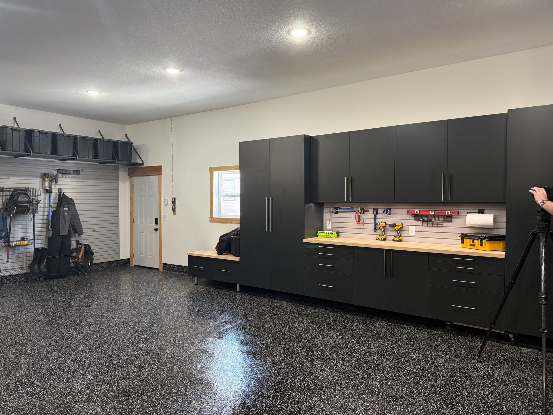 Spacious garage with black cabinets, workbench, and speckled epoxy floor; a ladder stands near the wall.