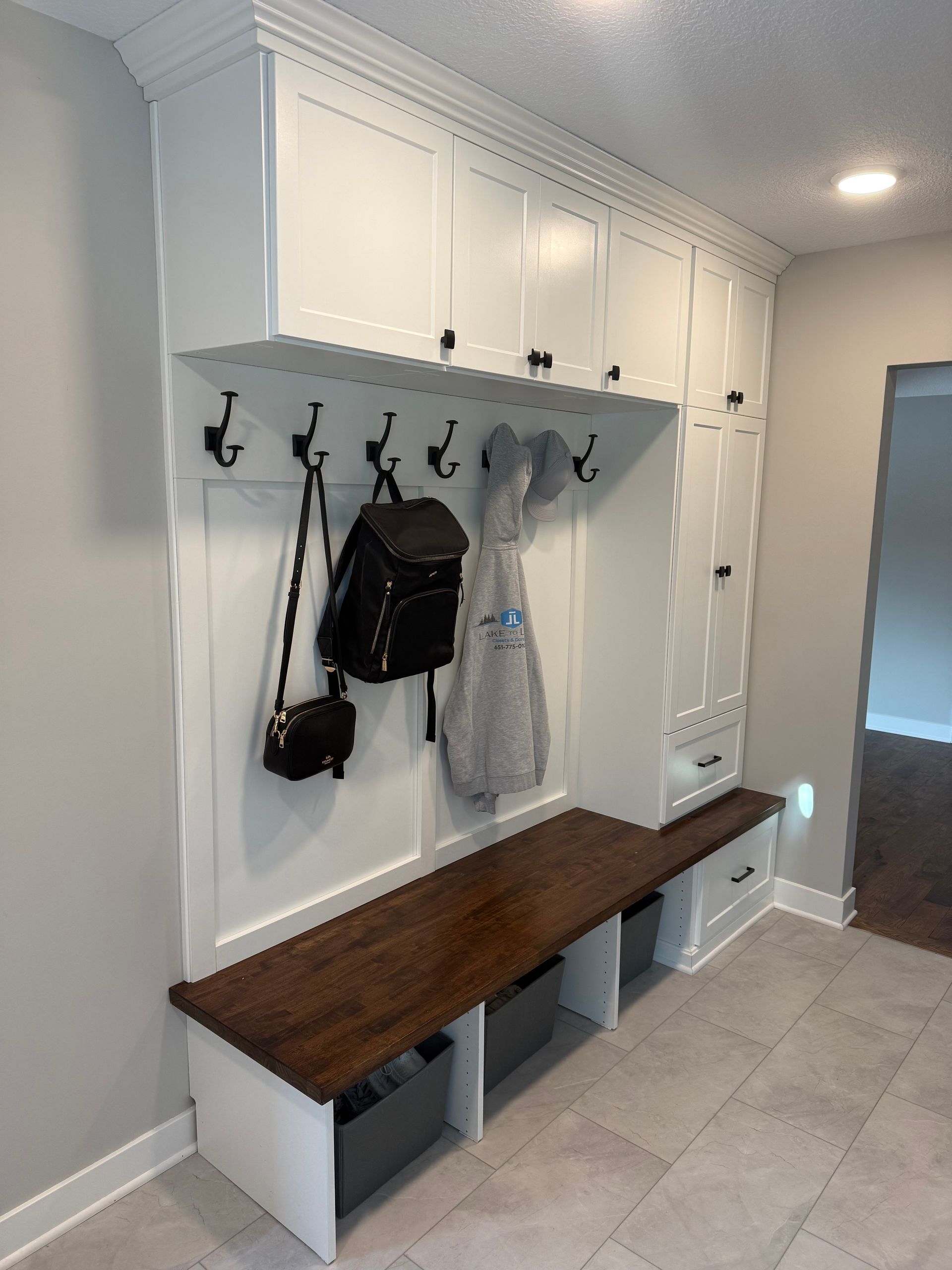 White entryway mudroom with hooks, bench, cabinets, and hanging bags and jackets