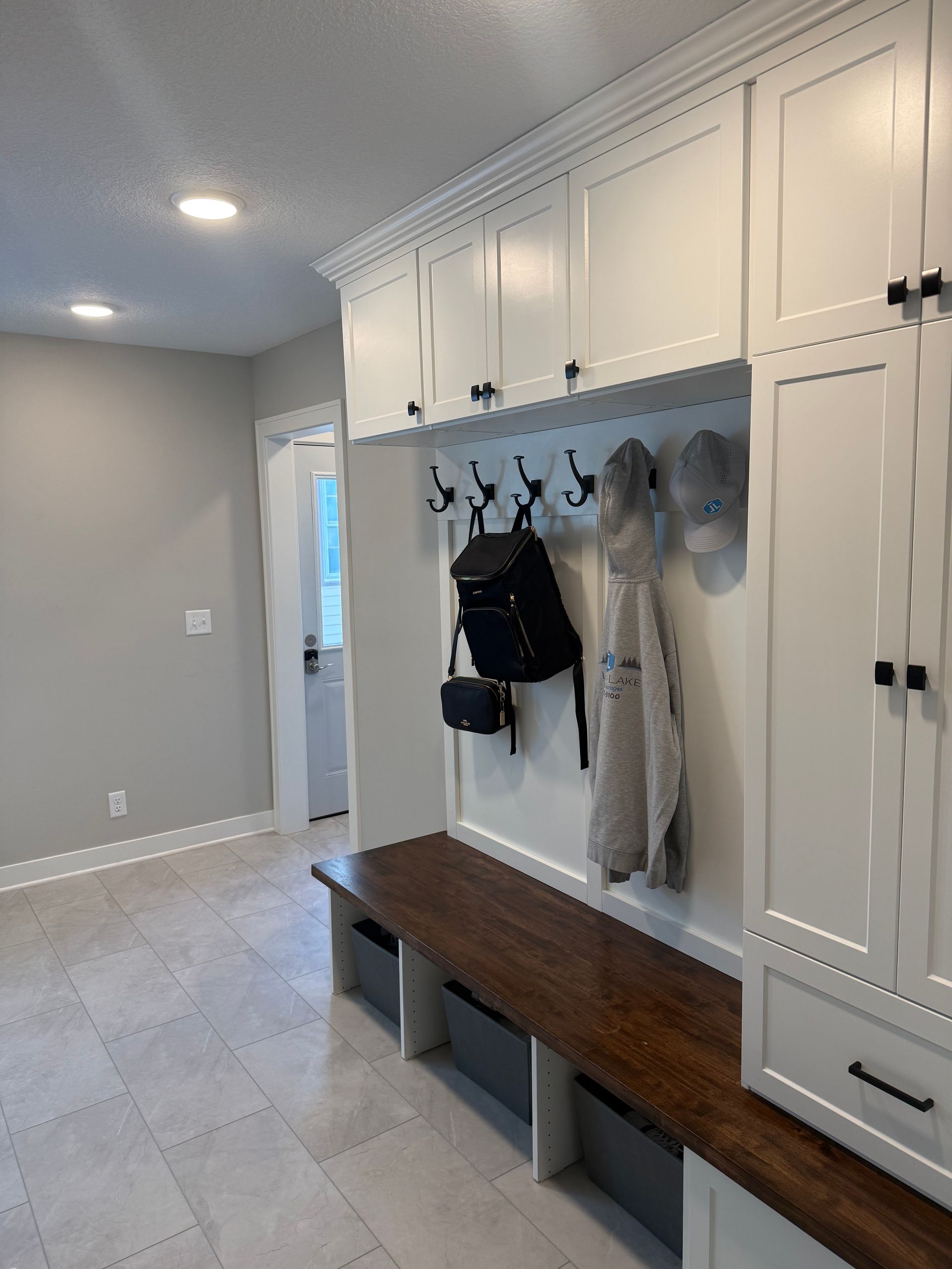 Entryway mudroom with white built-in lockers, hooks, bench, and tiled floor