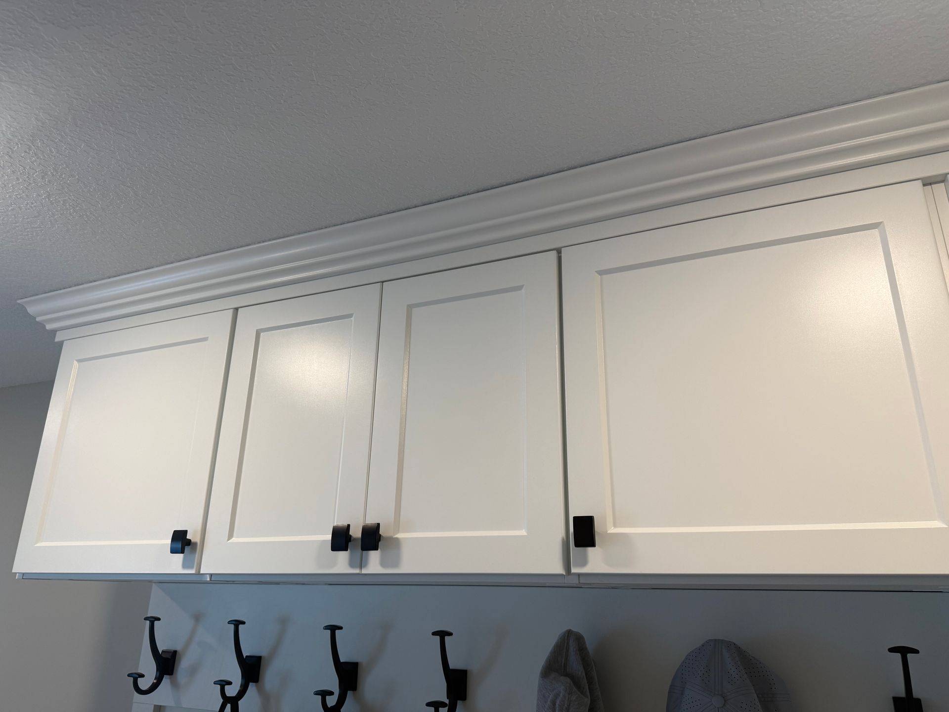 White kitchen cabinets with black handles above a row of black hooks on a wall