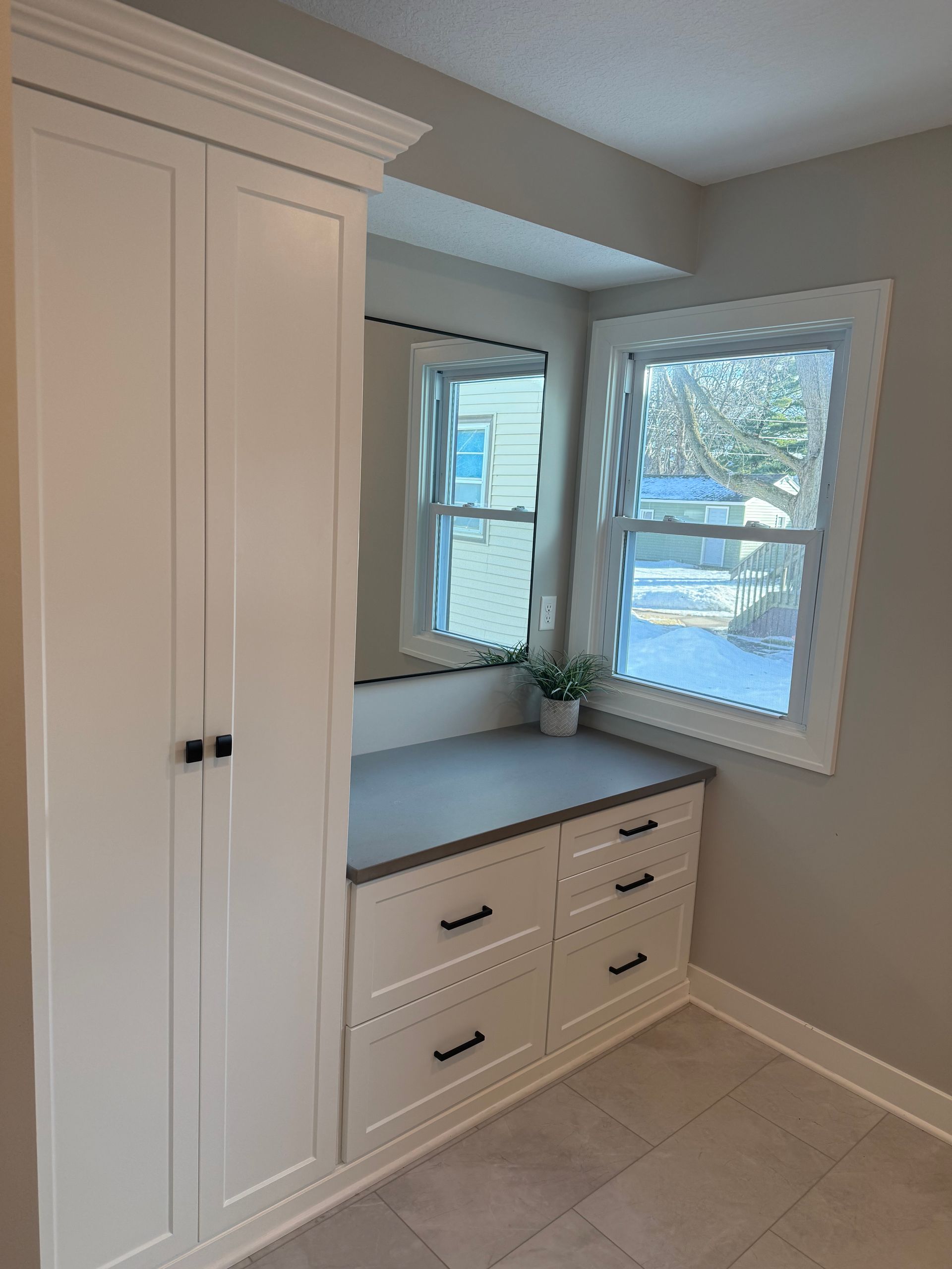 Built-in white cabinets and drawers beside a small window nook in a bright room