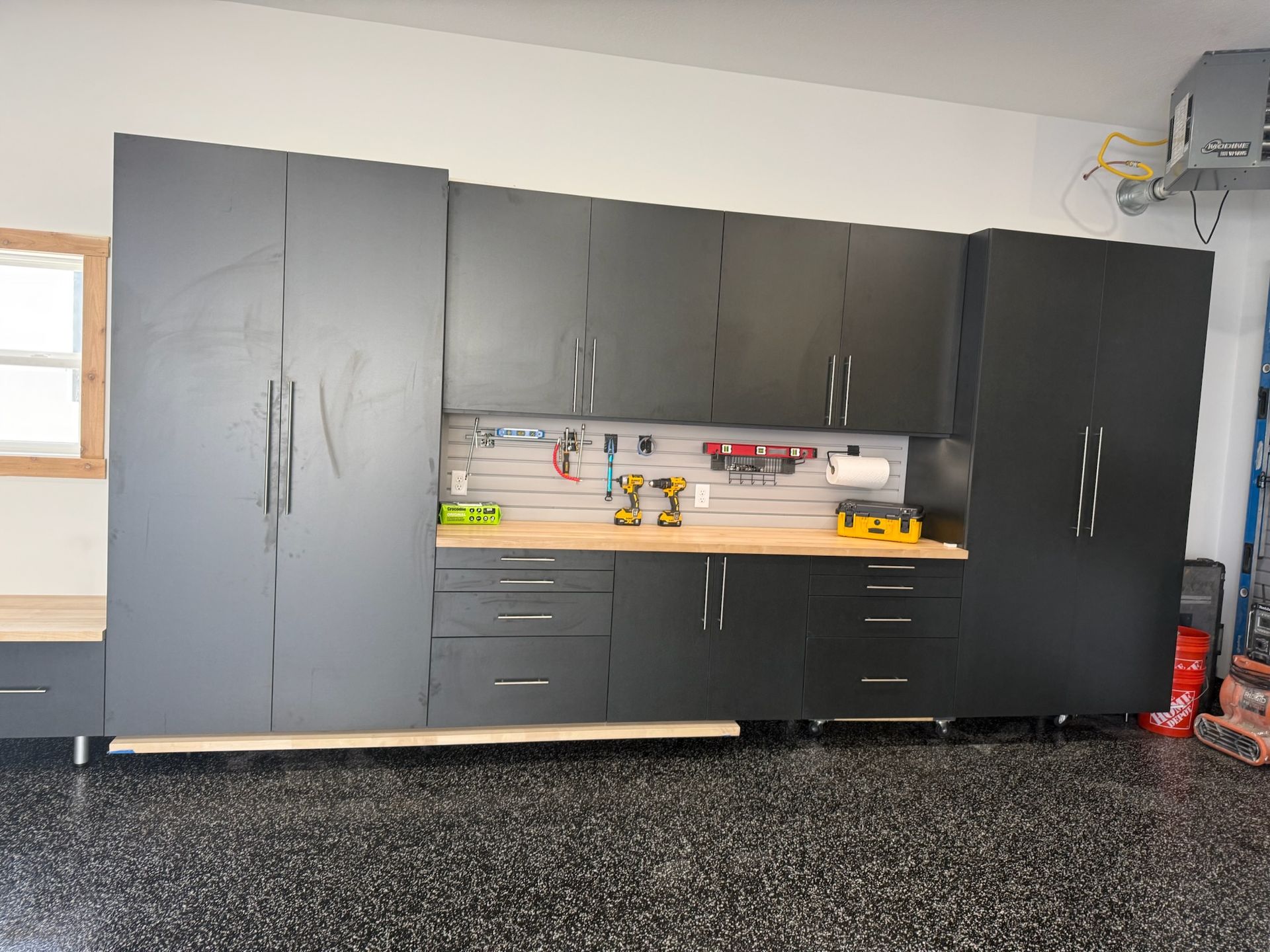 Large black and gray cabinets and workbench in a garage or workshop with a speckled floor
