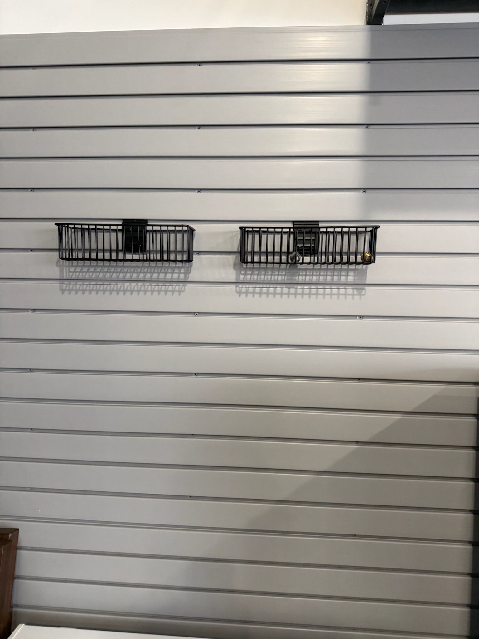 White slatted wall with two black wire baskets mounted side by side.