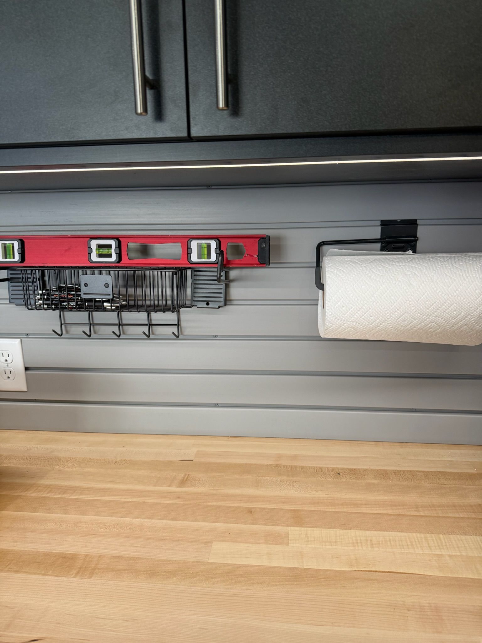 Garage wall with red level, hanging tools, and a paper towel roll beneath dark cabinets
