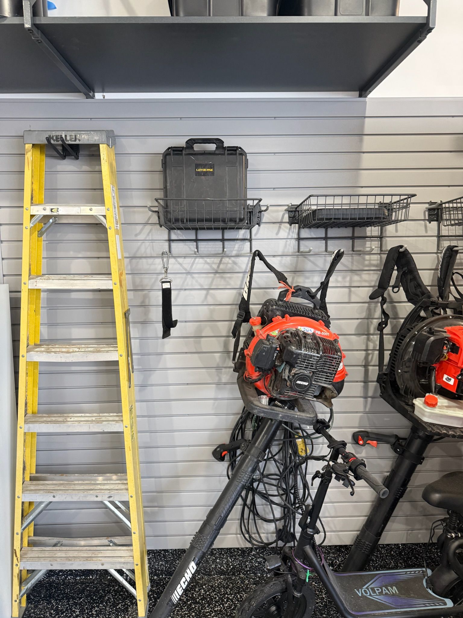 Ladders and motorcycle gear displayed in a shop corner with black shelving and hanging equipment.
