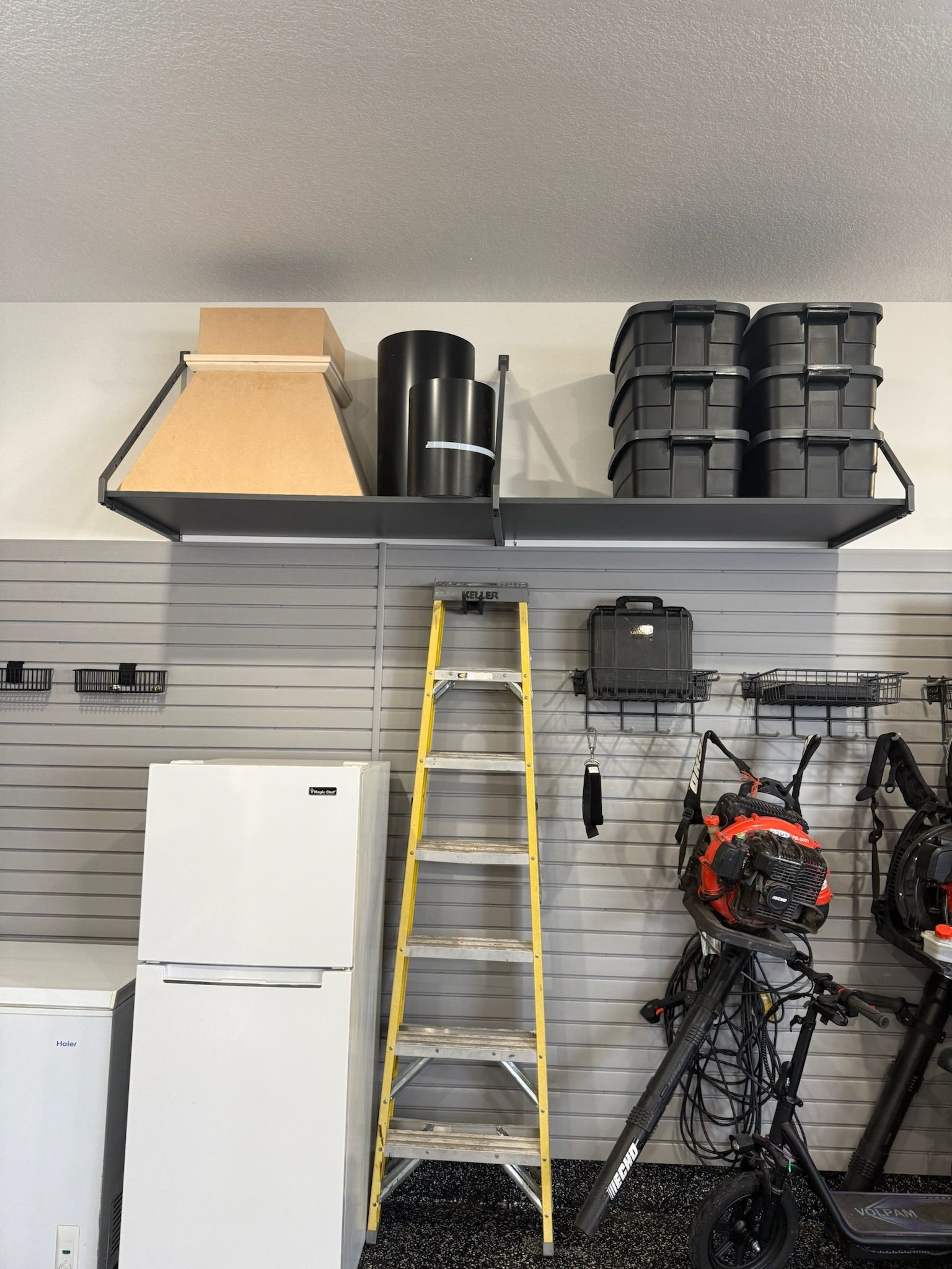 Garage storage with a yellow ladder, white refrigerator, shelves of bins, and hanging tools and bikes