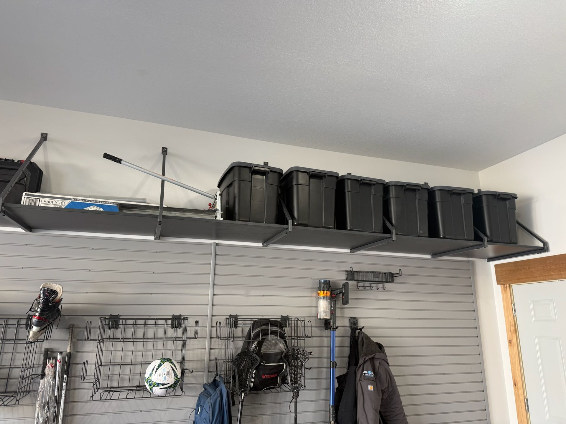 Garage wall with mounted shelves, black storage bins, and hanging tools/gear on pegboard hooks.