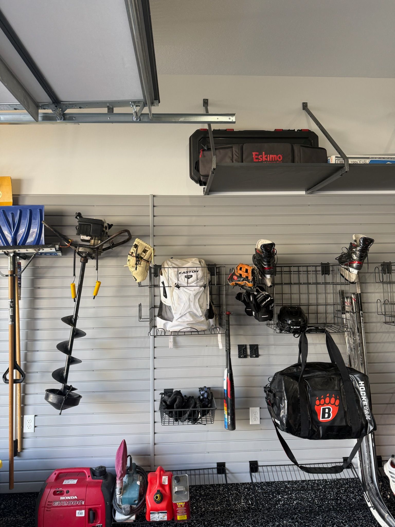 Garage wall with organized power tools, hanging equipment, and storage shelves under the ceiling.