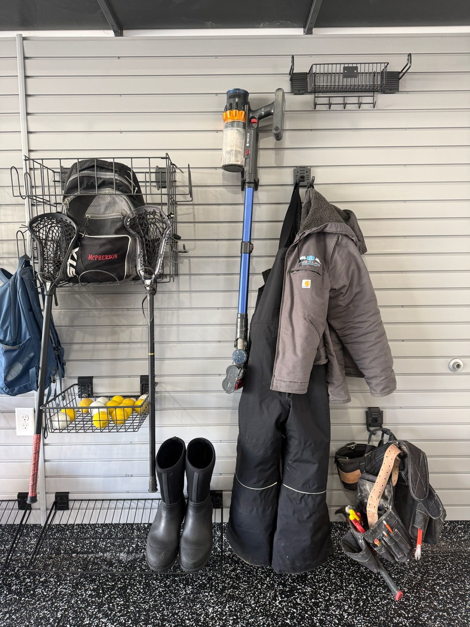 Wall-mounted winter gear display with coats, boots, helmets, and gloves in a garage or entryway.