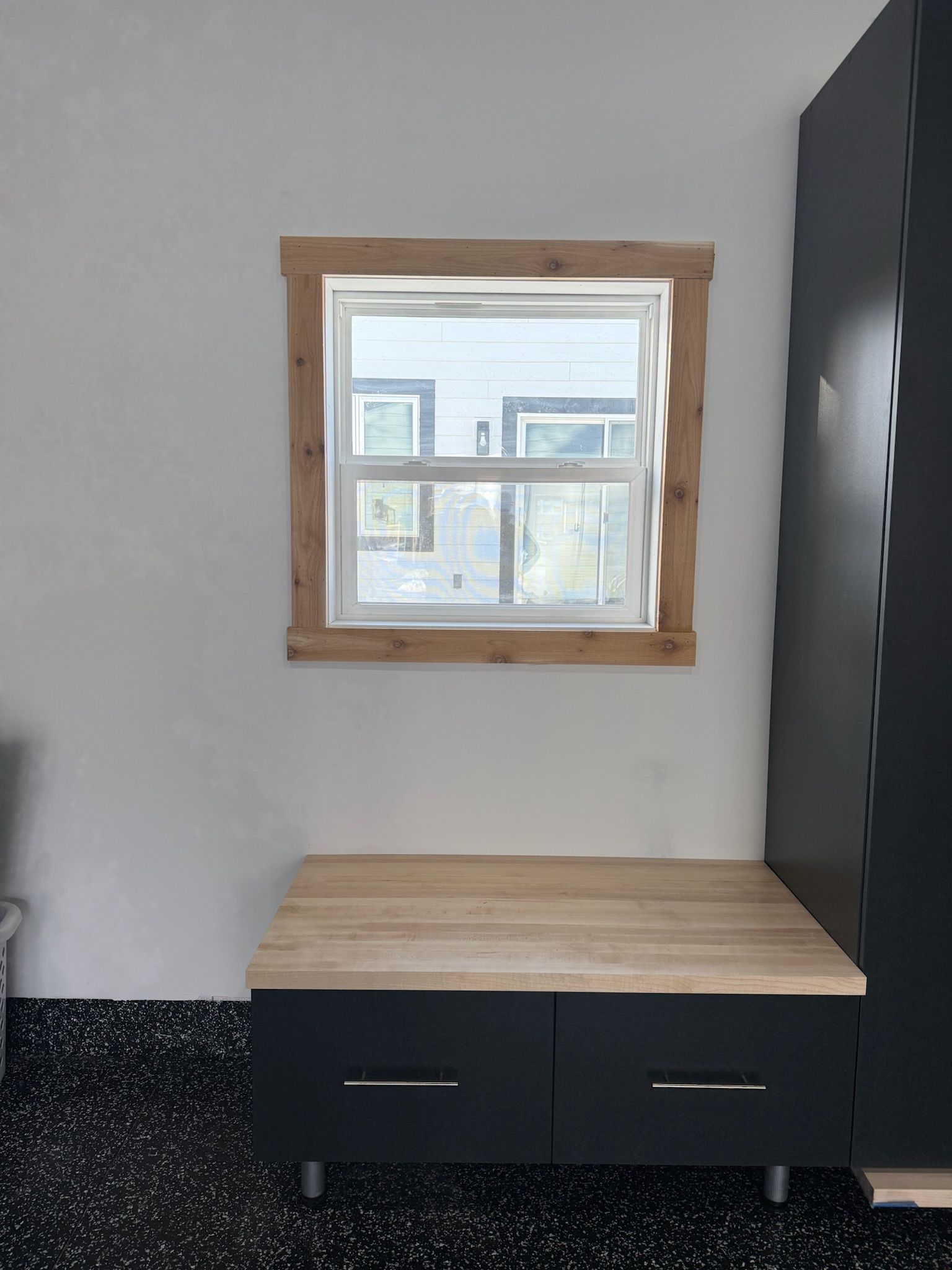 Small room nook with a window above a light wood bench and black drawers against gray walls.