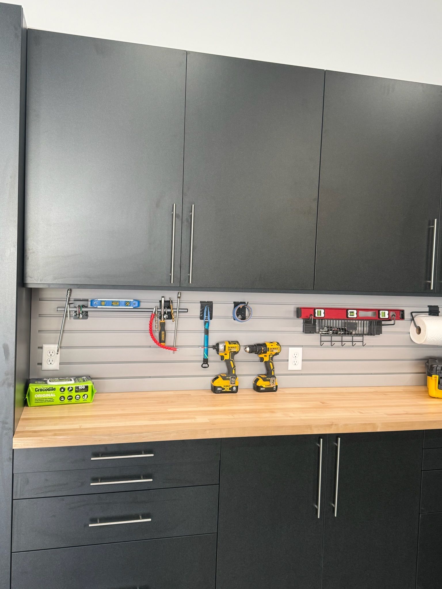 Garage workbench with black cabinets, wooden countertop, and neatly arranged power tools and accessories.