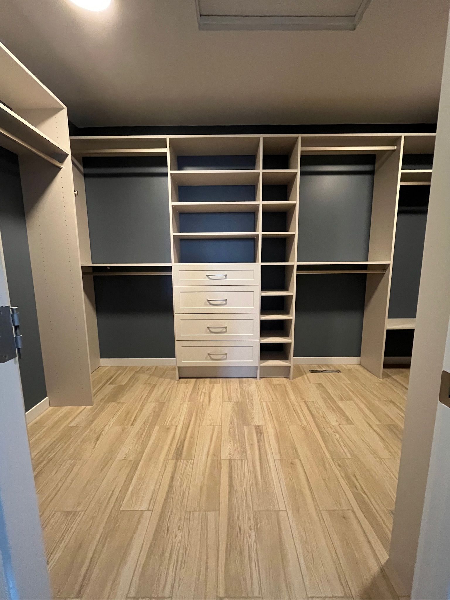Empty walk-in closet with wood floor, gray built-in shelving, and central white drawers.
