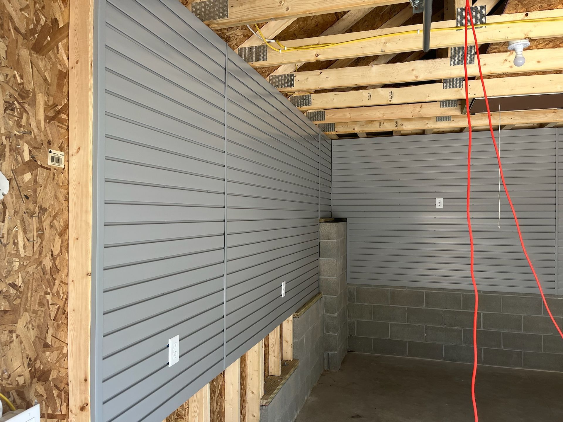 Interior under construction with gray slat walls, exposed ceiling joists, and cinder block walls.