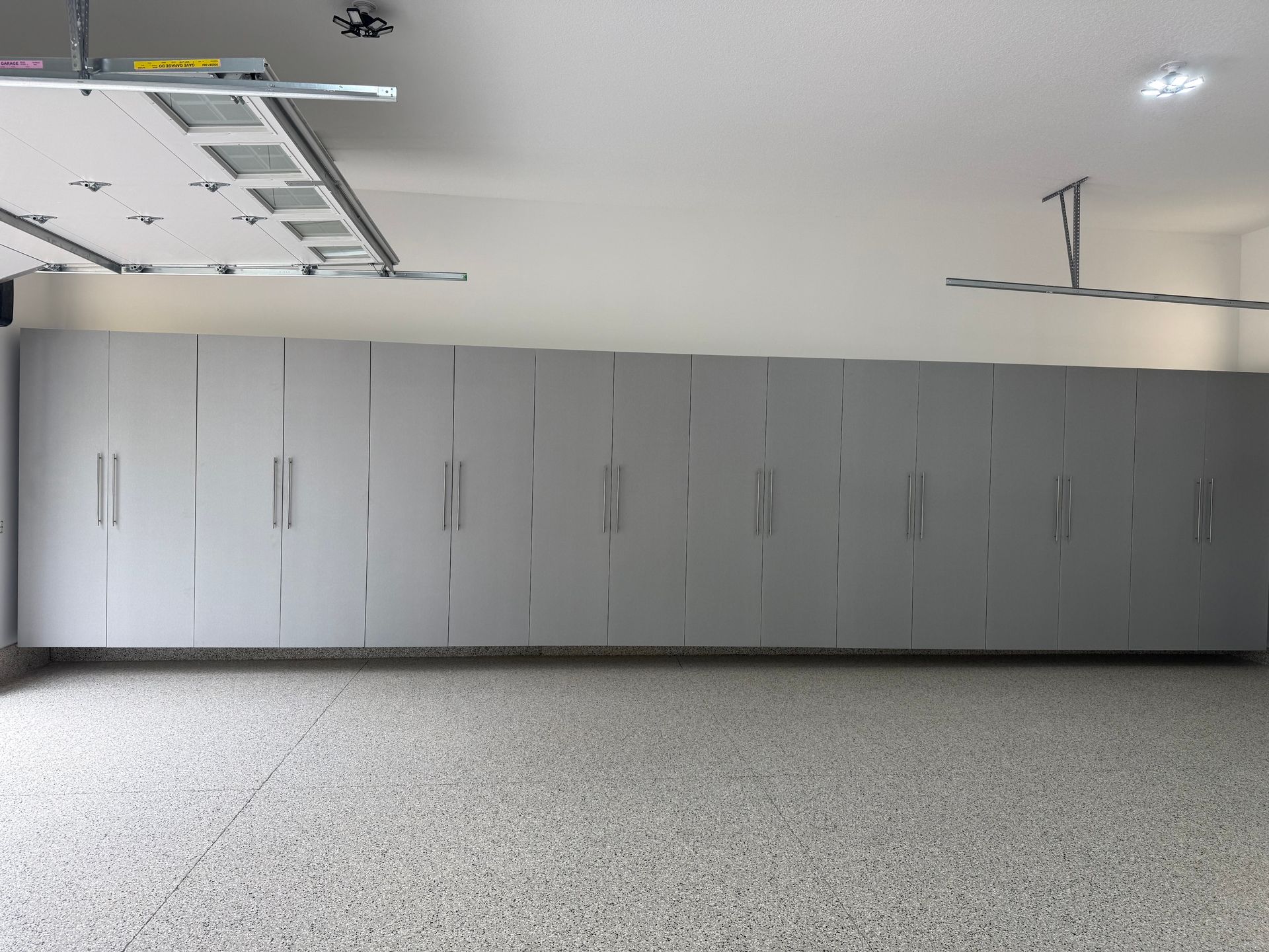 Large gray storage cabinets line a clean garage wall with a speckled floor and overhead light.