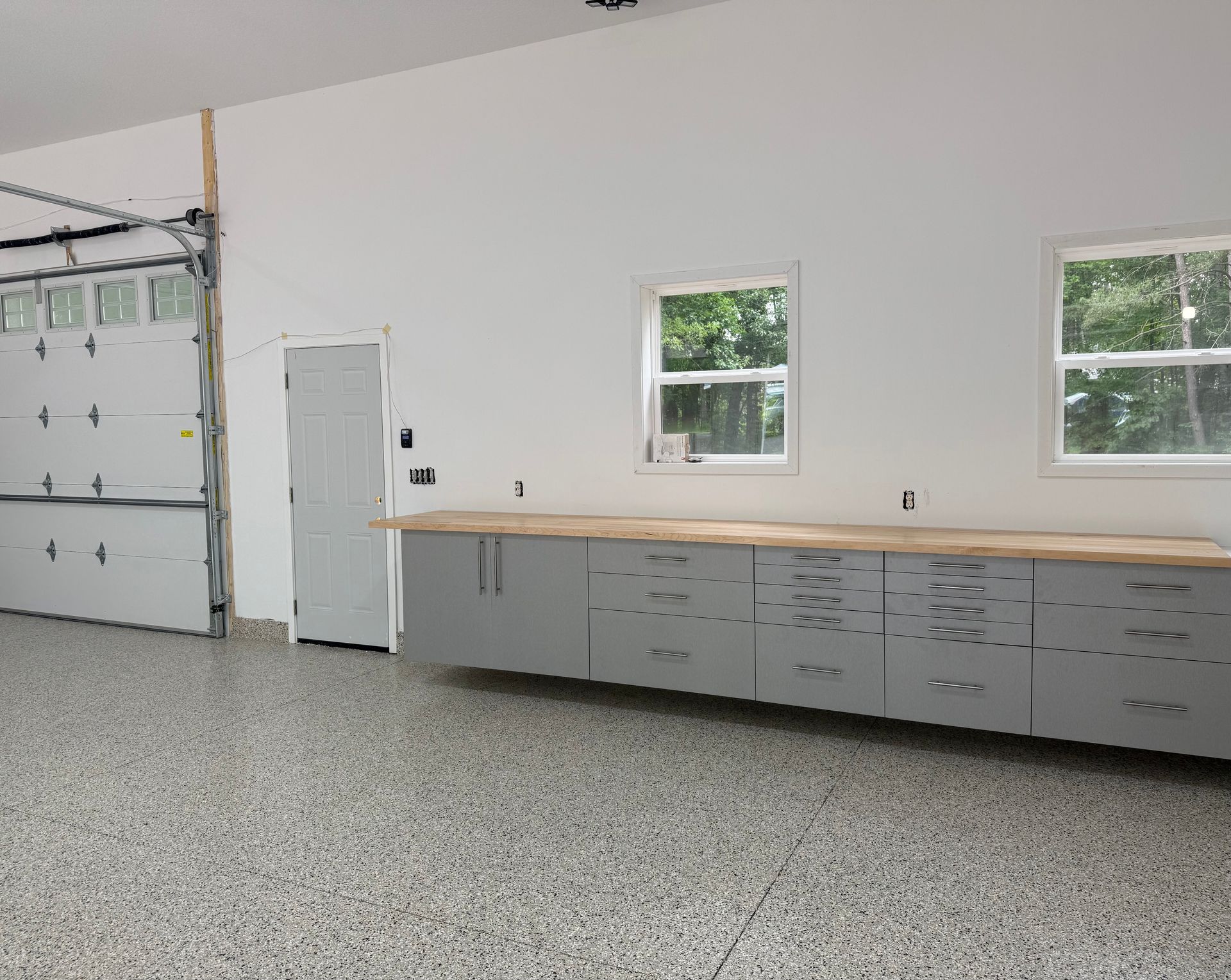 Spacious garage with gray cabinets, windows, and a side door on a speckled floor