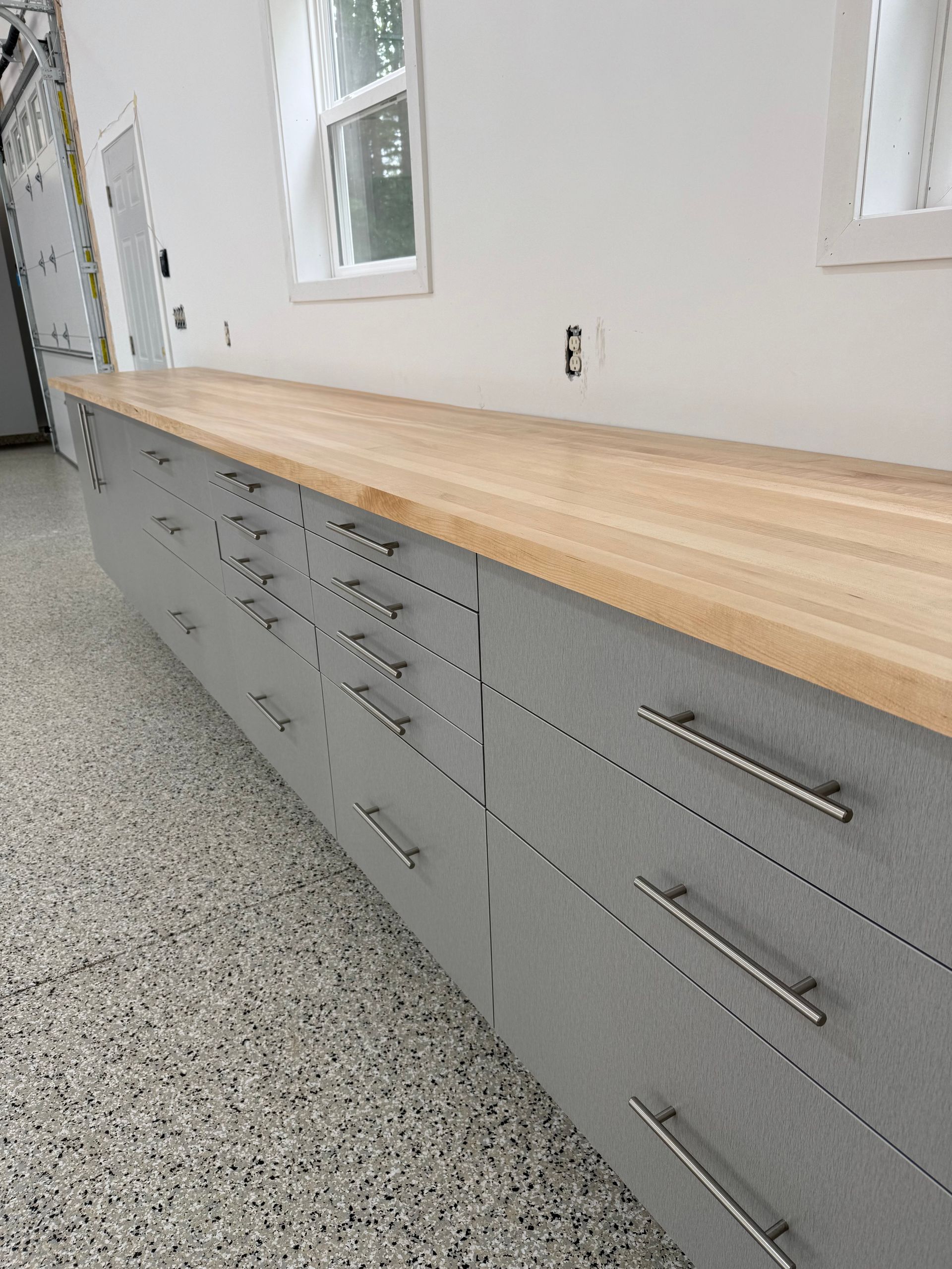 Long gray cabinet with wood countertop in a bright room with windows.