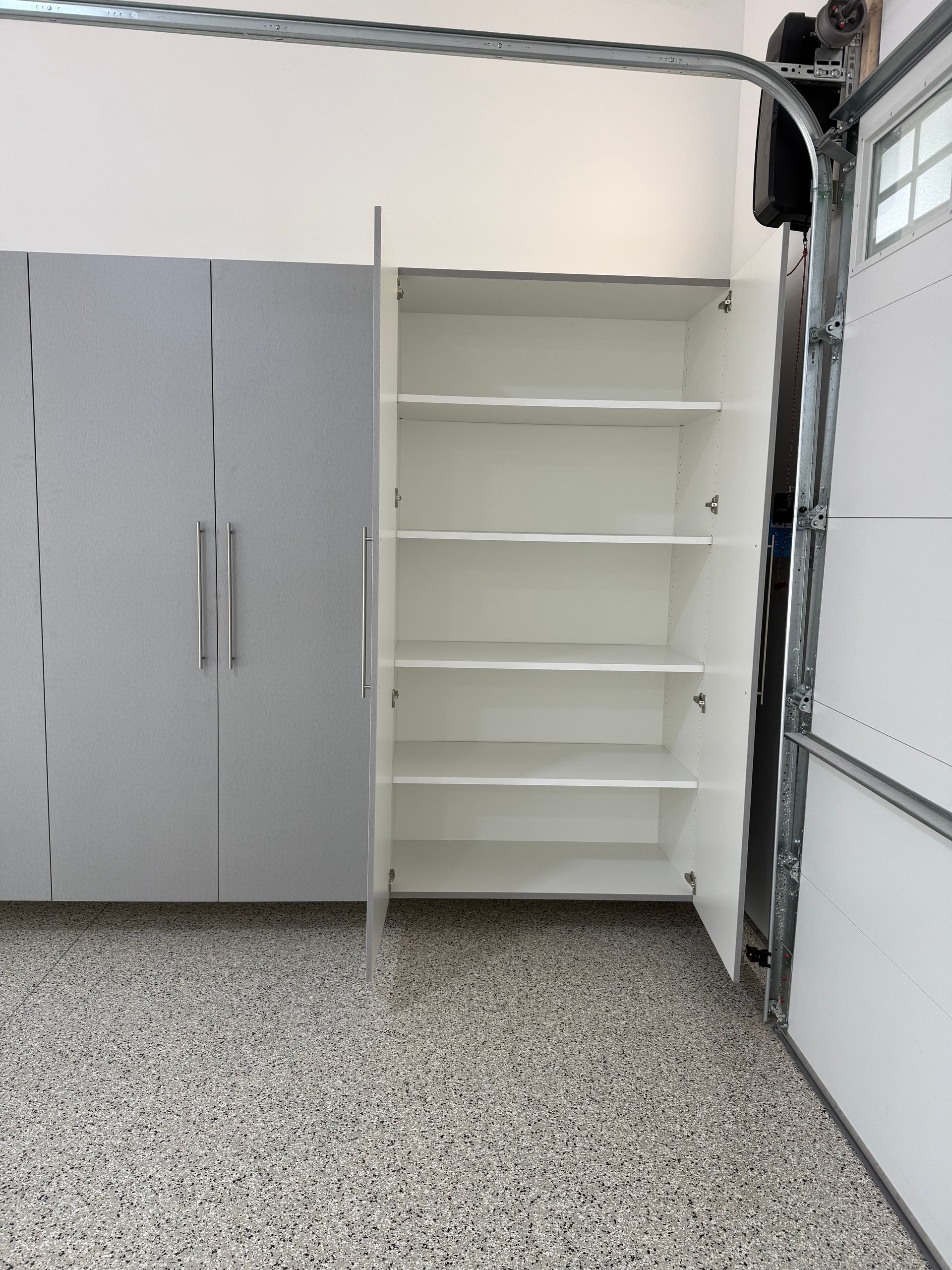 White shelving unit beside gray storage cabinets in a garage with a speckled floor