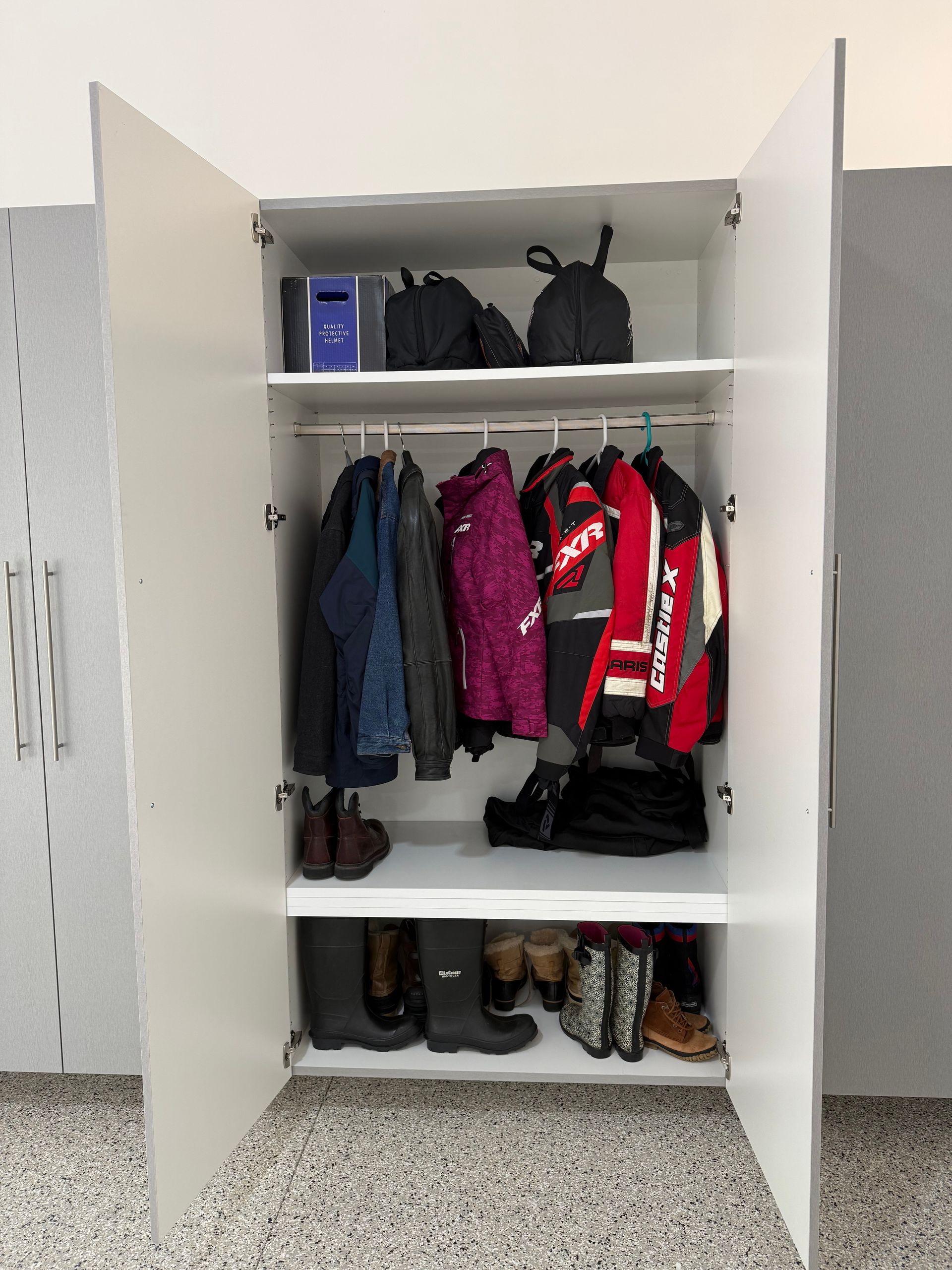 Open white school locker with coats, backpacks, and shoes on shelves and floor.