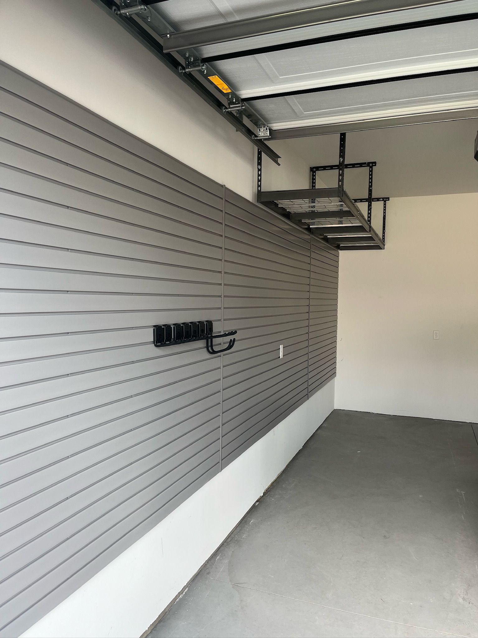 Empty garage with gray slatwall, wall-mounted storage rack, and concrete floor.