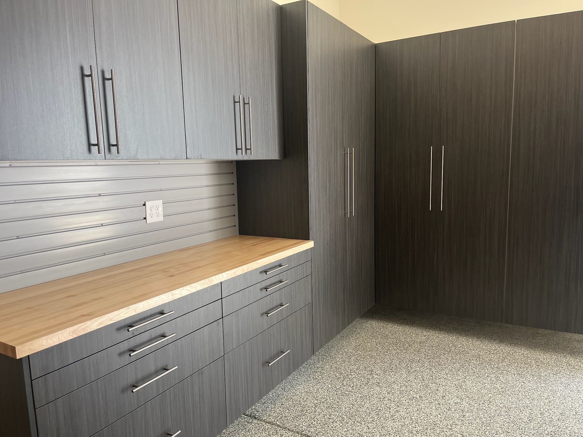 Gray built-in cabinets and wood countertop in a modern storage room with a speckled floor.