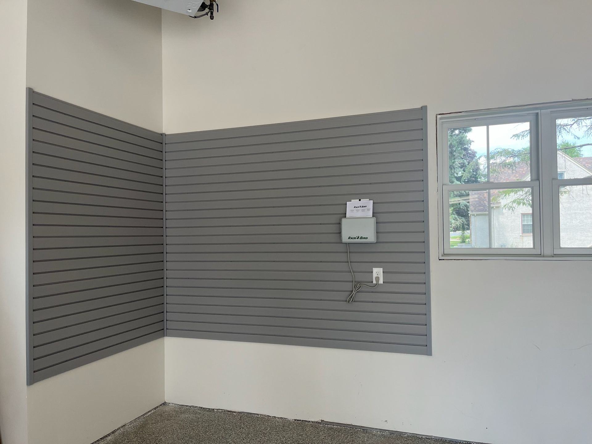 Empty room corner with gray slatwall panels, a window, and a small wall-mounted shelf.