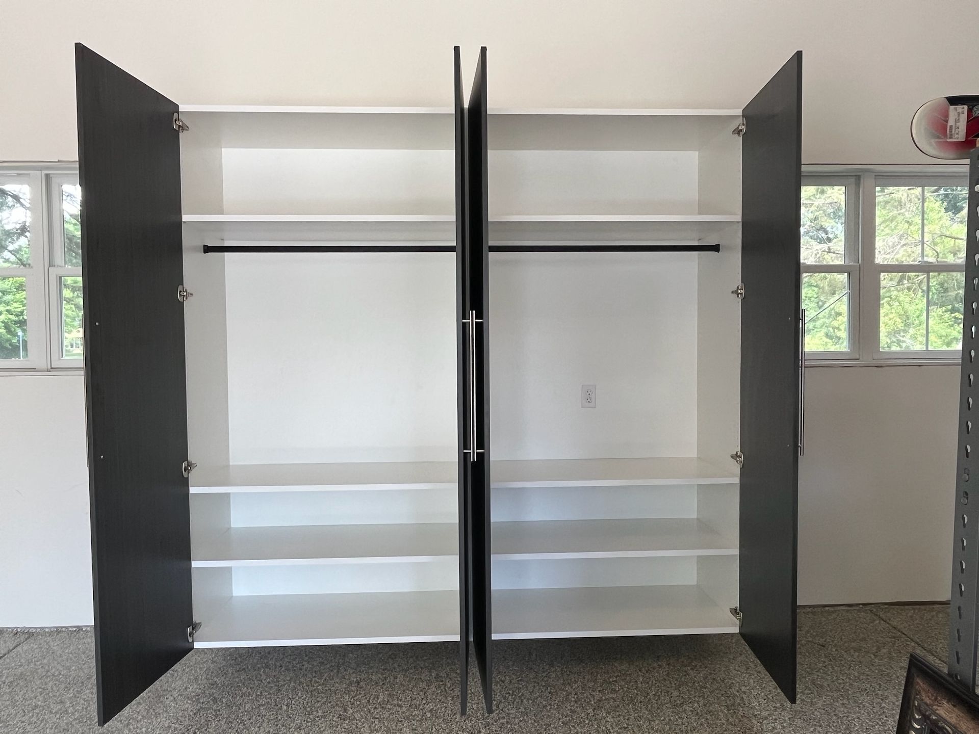 Open wardrobe with dark doors, shelves, and hanging rods in a bright room