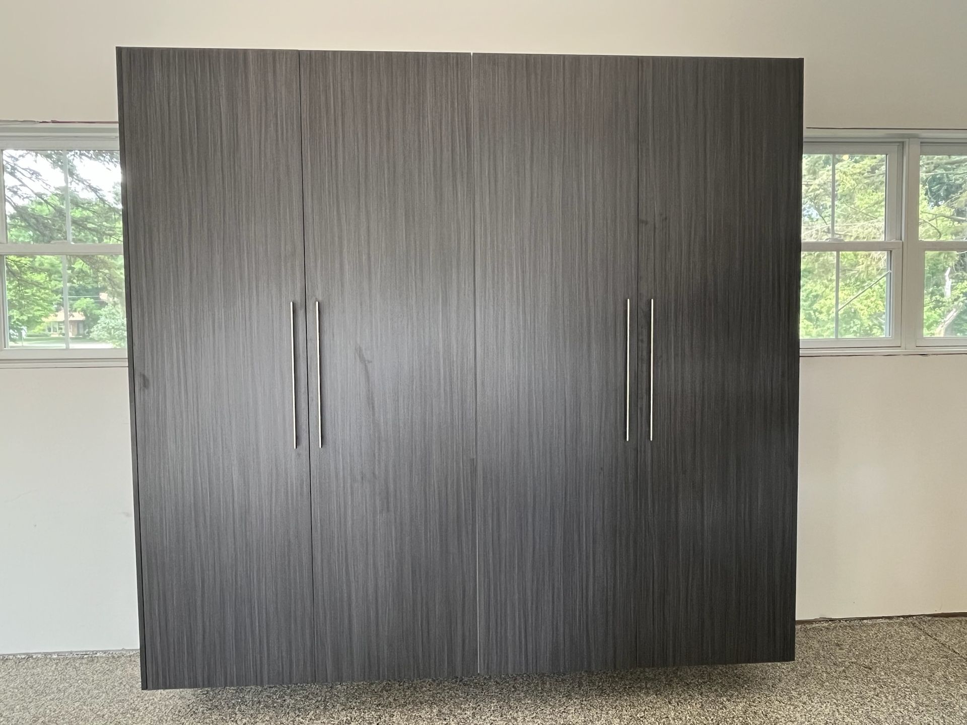 Large dark wood wardrobe with silver handles standing against a white wall beneath windows