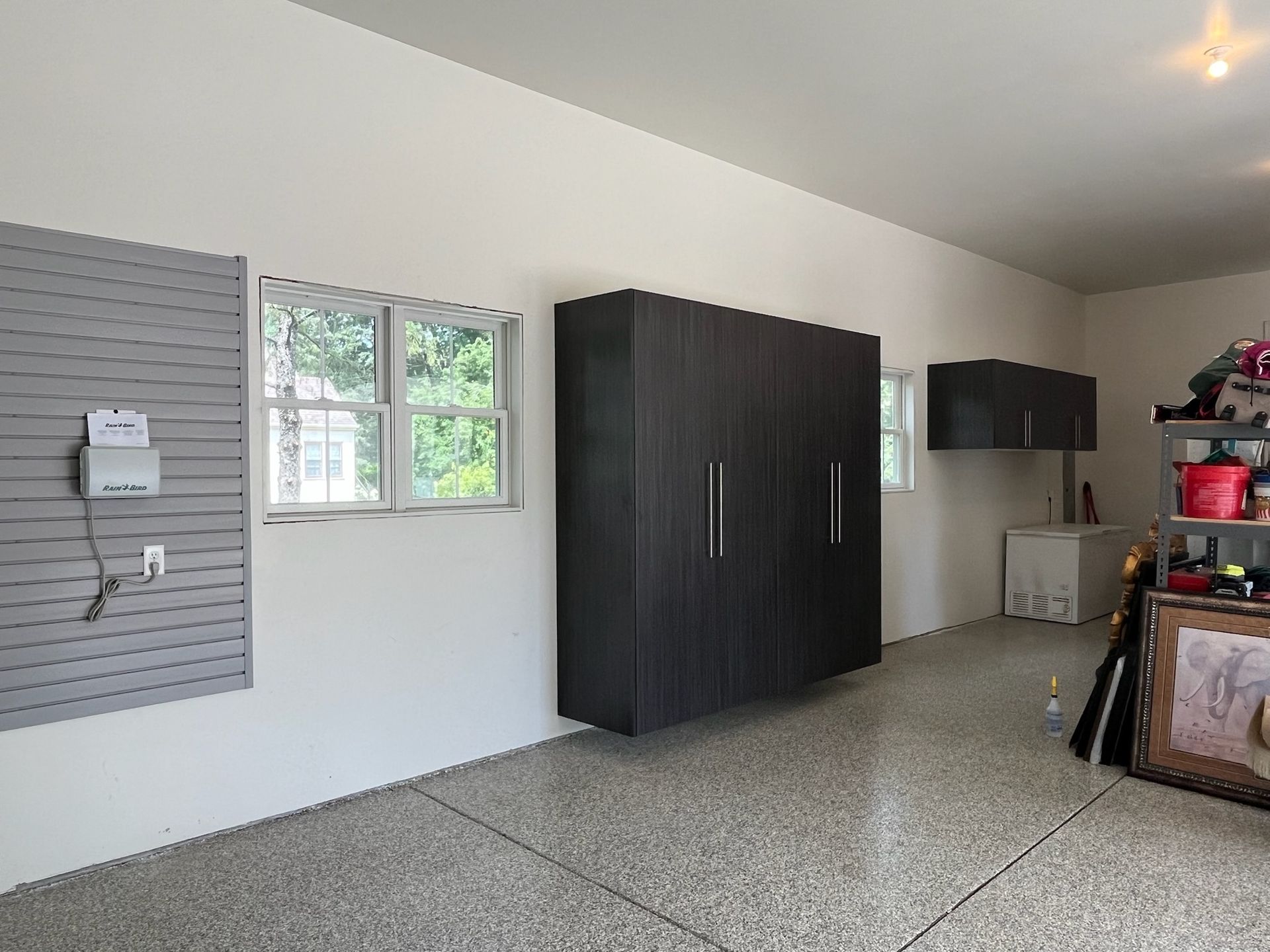 Garage with gray floor, dark cabinets, and a windowed wall in a tidy storage area