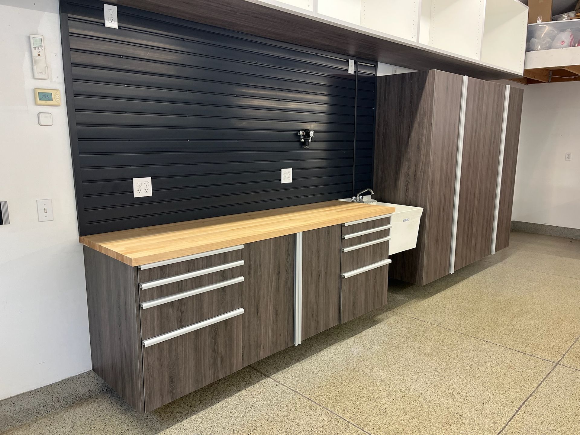 Modern kitchenette with dark wood cabinets, wooden countertop, black backsplash, and tall pantry cabinets.