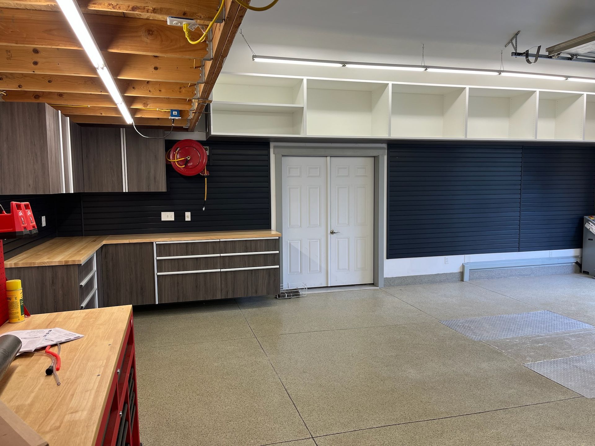 Empty room with dark cabinets, white double doors, and gray epoxy floor under wood ceiling beams