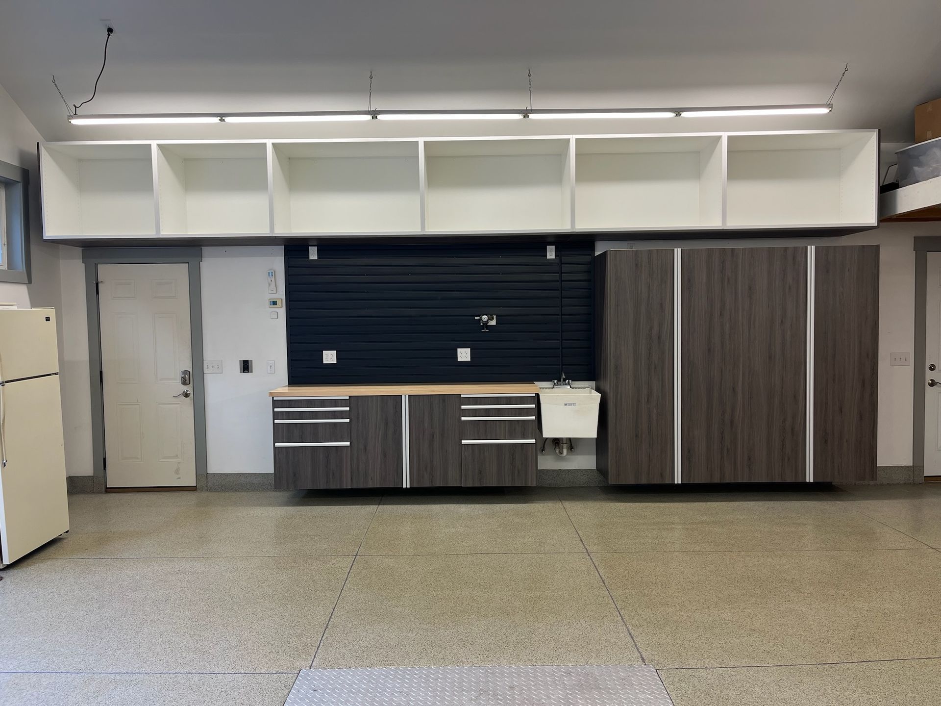 Empty classroom wall with cabinets, shelves, and a counter under fluorescent lights