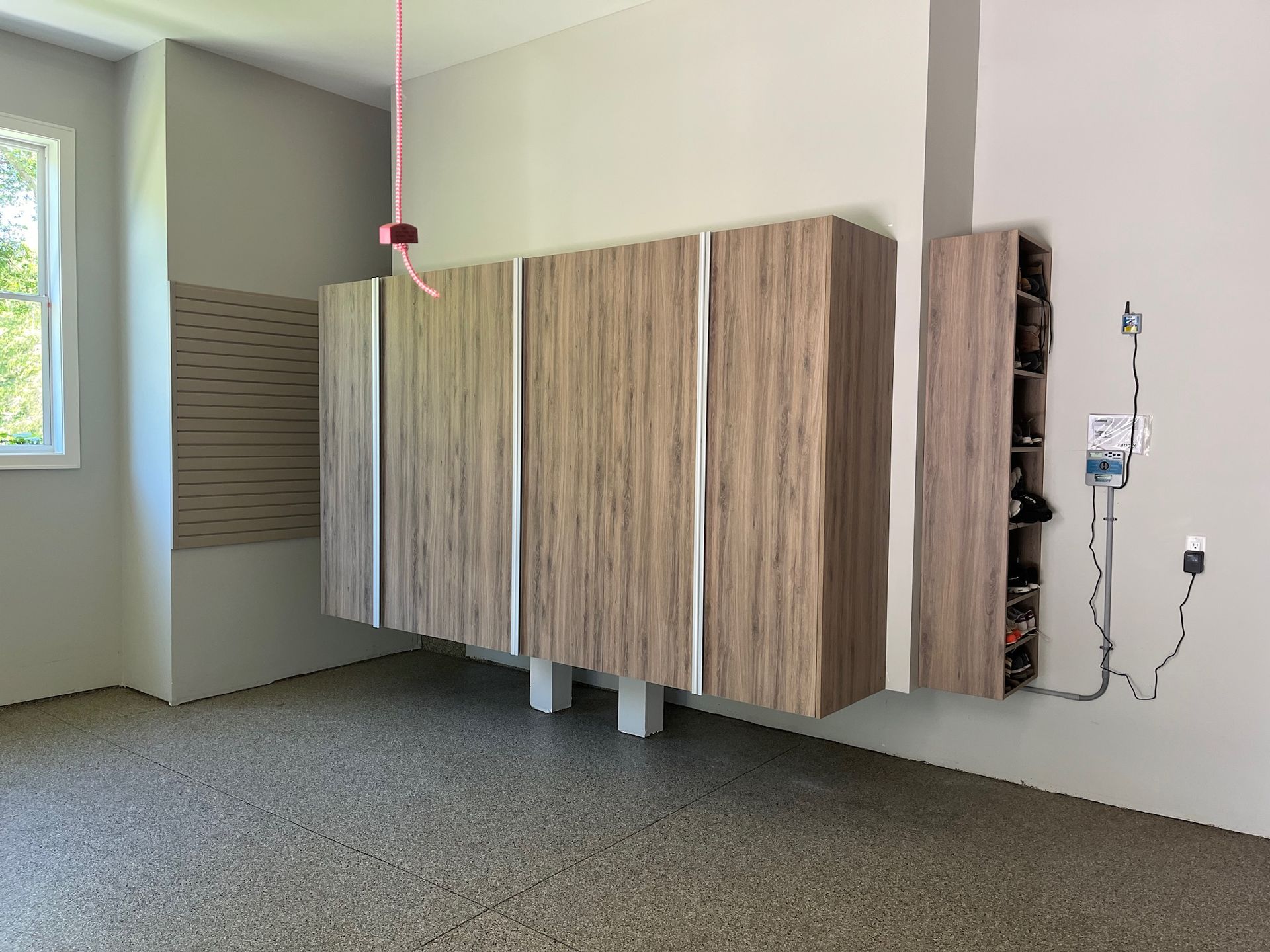 Modern room with wood-grain wall cabinets, window, and hanging cords on a white wall