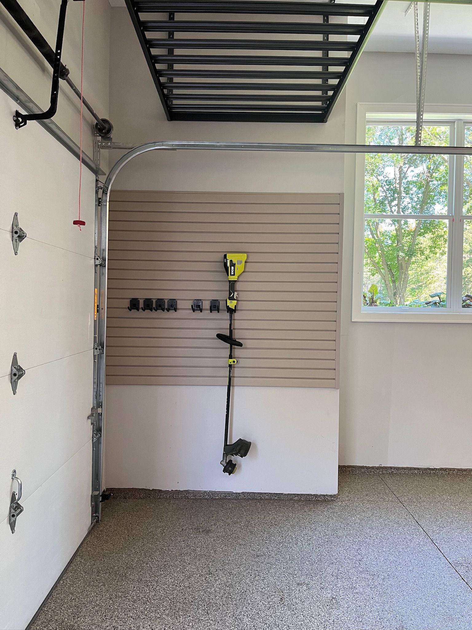 Garage interior with a wall-mounted power tool organizer, pegboard, overhead storage, and a window on the right.