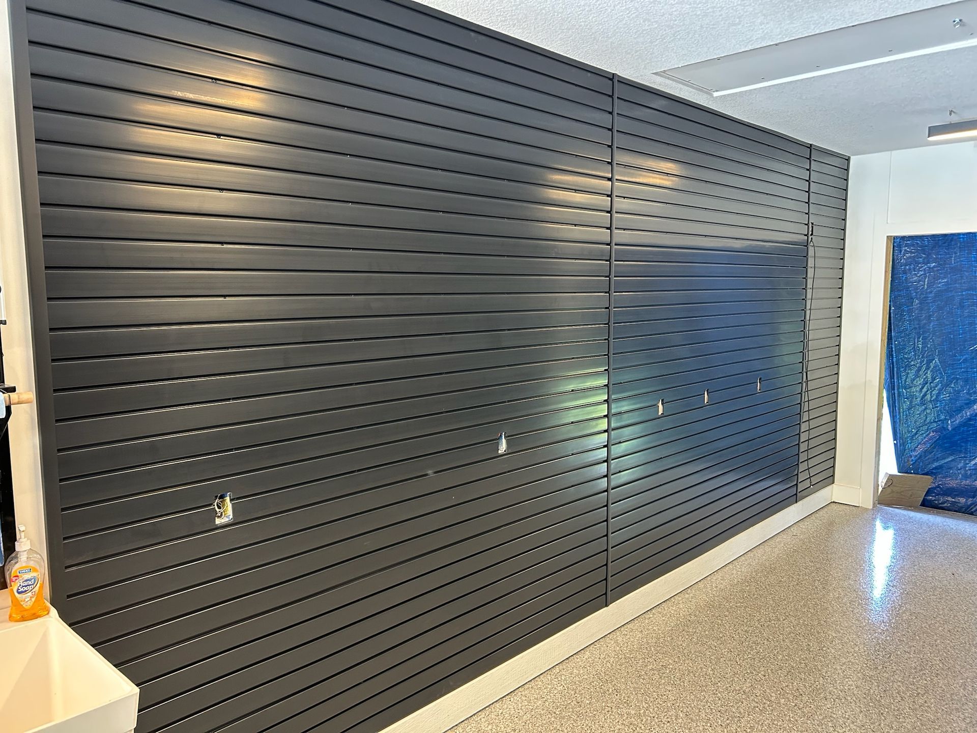 Black slat wall with a large dark glass panel in a bright indoor hallway