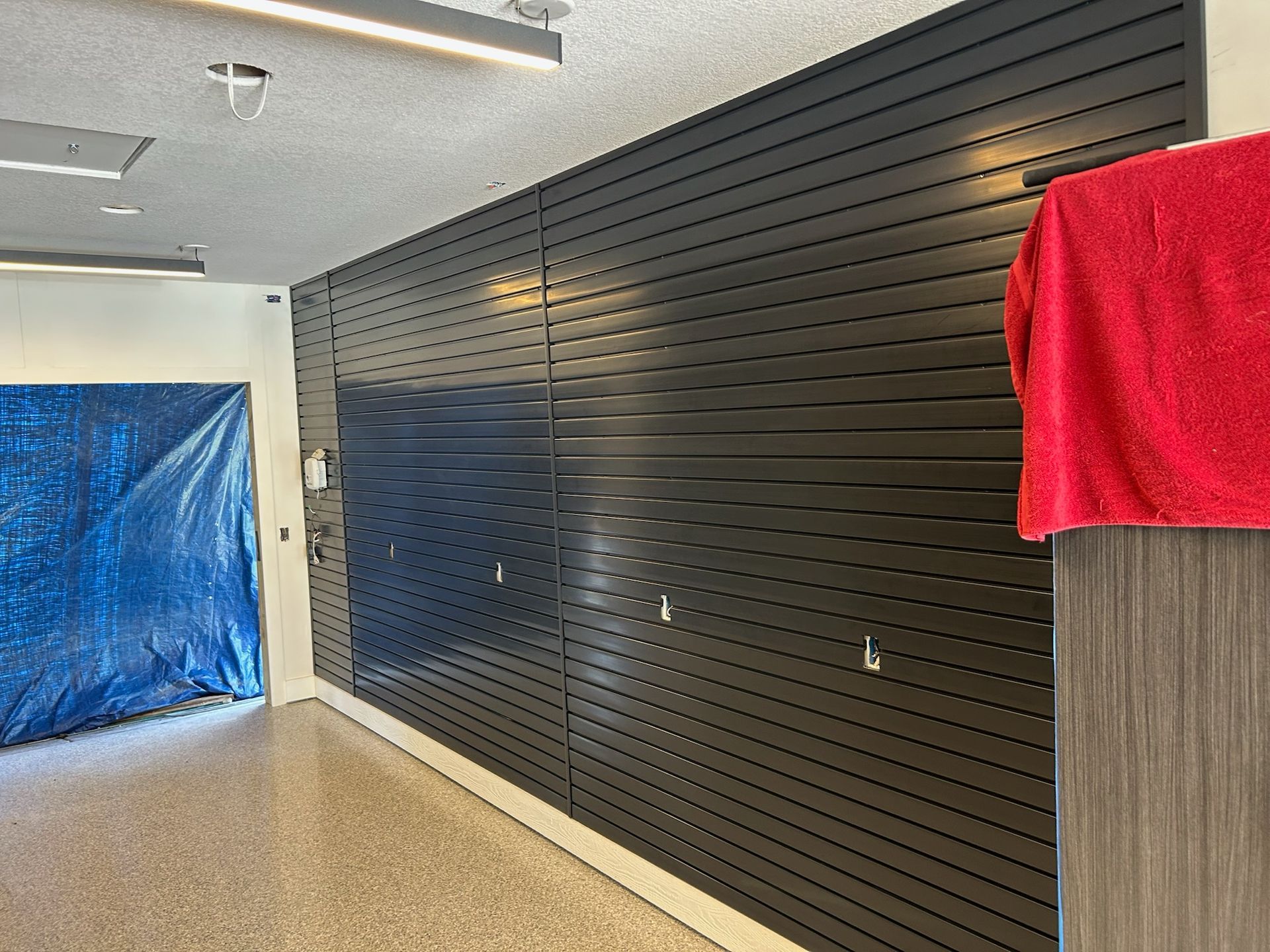 Empty retail space with black slat wall, blue-covered doorway, and red cloth draped over a partition.