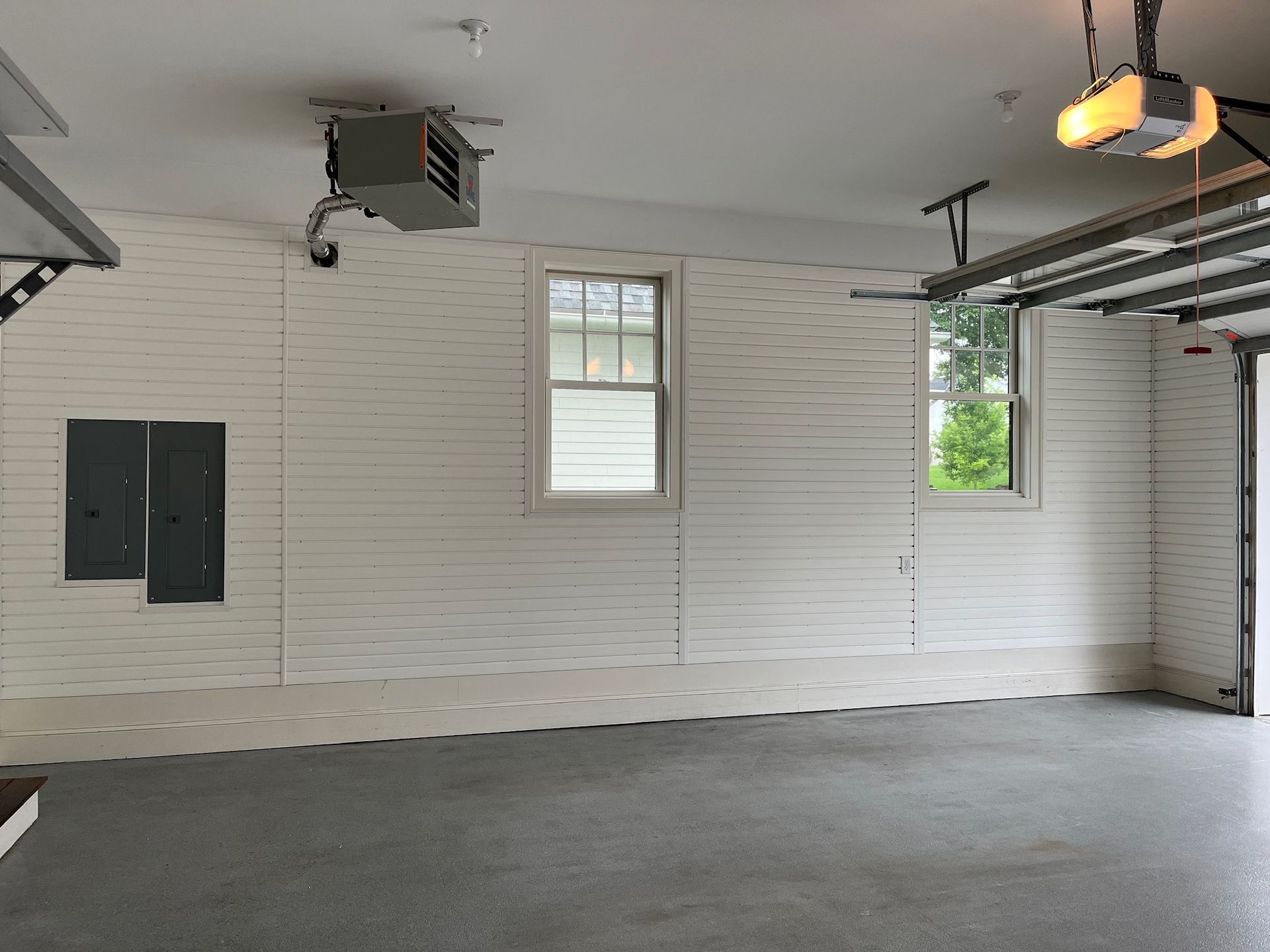 Empty garage interior with white paneled walls, gray floor, windows, and overhead door rails