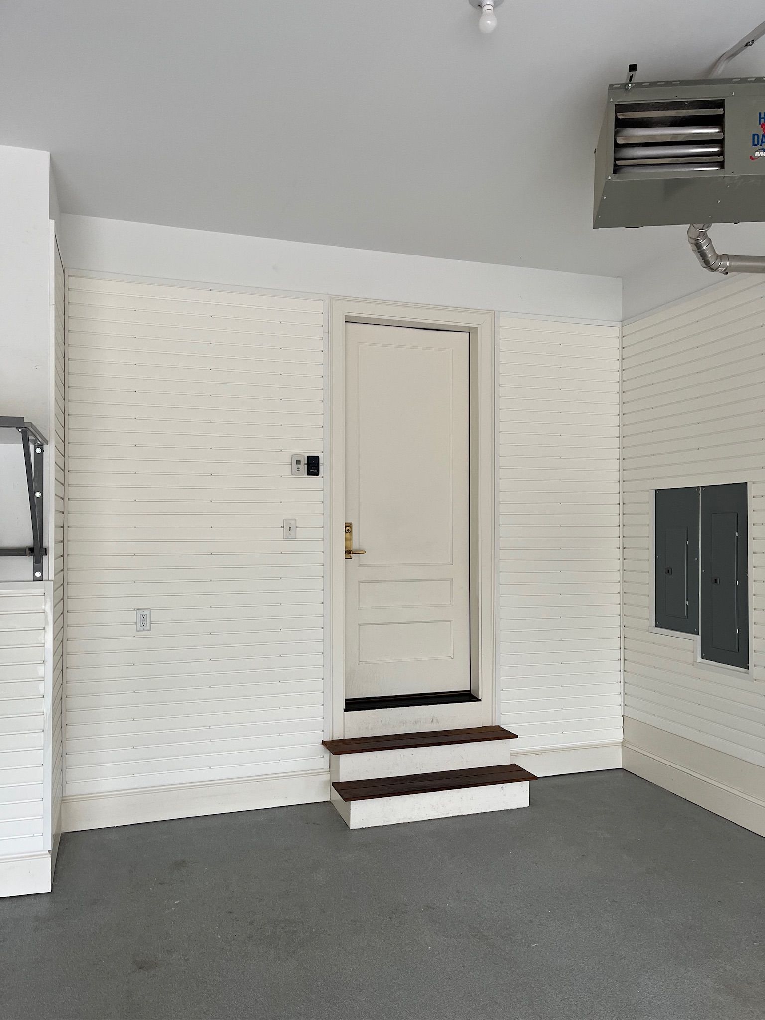 Garage interior with a white door on steps, gray carpet, and wall-mounted storage panels.