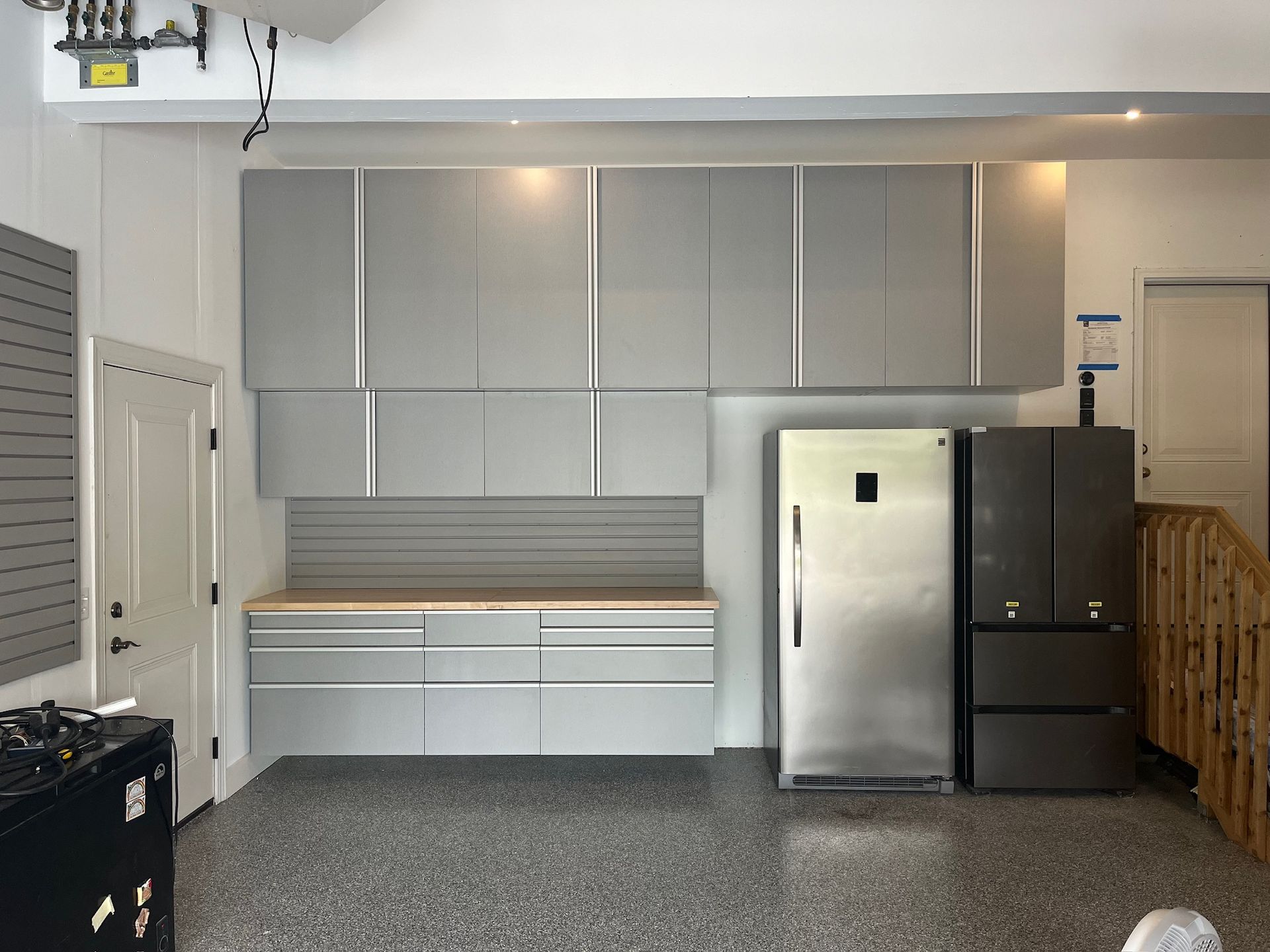Empty garage workspace with gray cabinets, stainless fridge, workbench, and storage bins