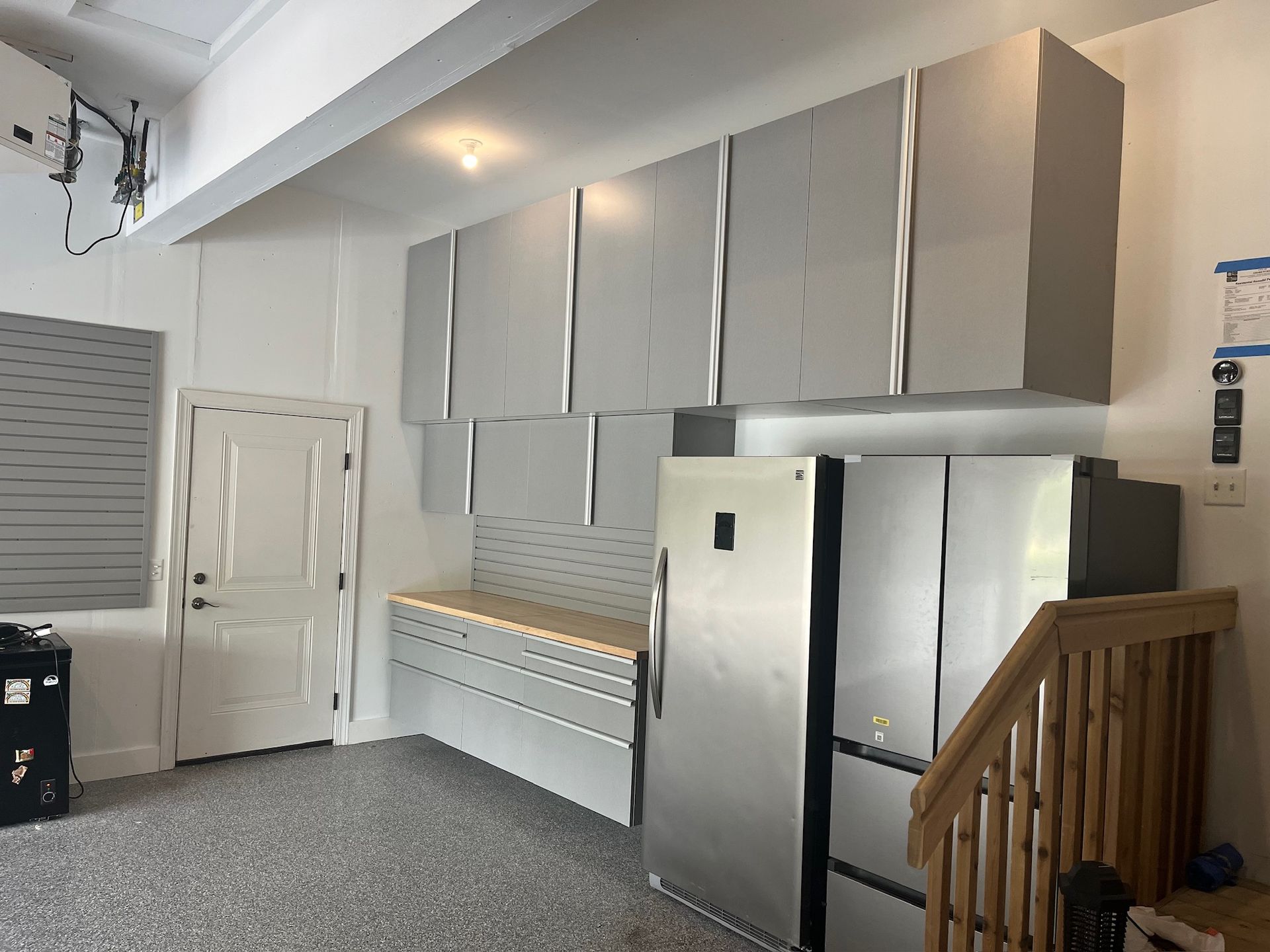 Modern kitchen with stainless steel appliances, gray cabinets, white door, and wood staircase railing
