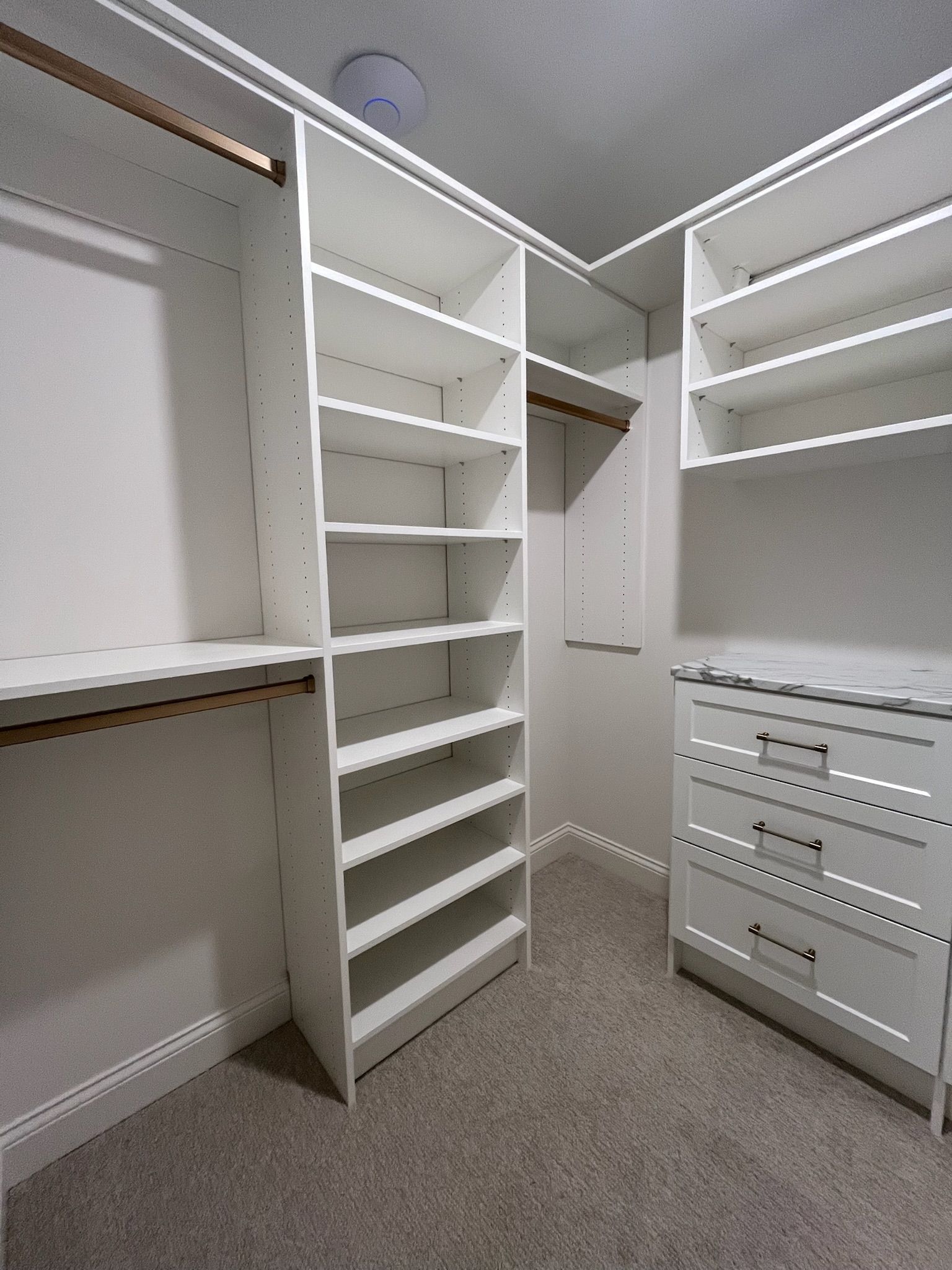 Empty white walk-in closet with shelves, hanging rods, drawers, and beige carpet.