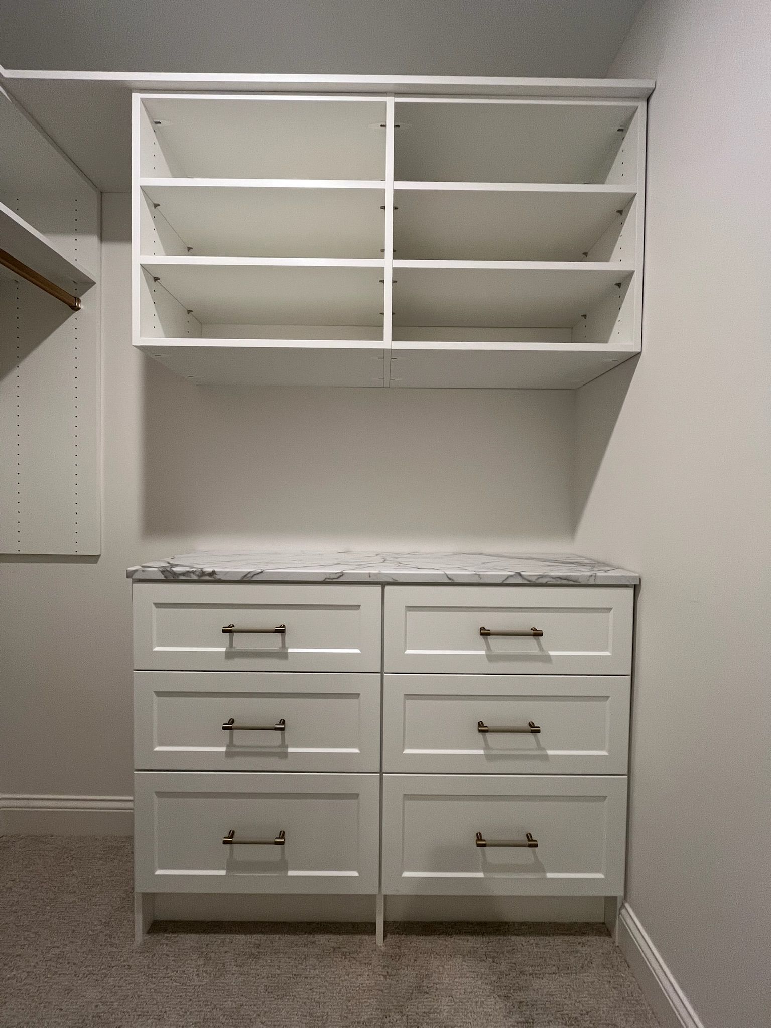 White built-in closet with open shelves above six drawers in an empty room.