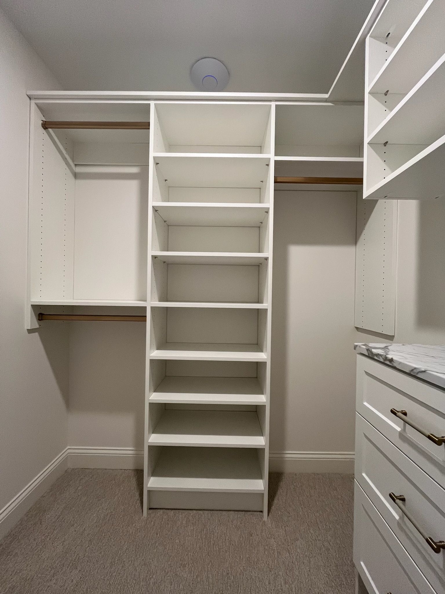 Walk-in closet with white shelving, hanging rods, drawers, and a central set of shelves.