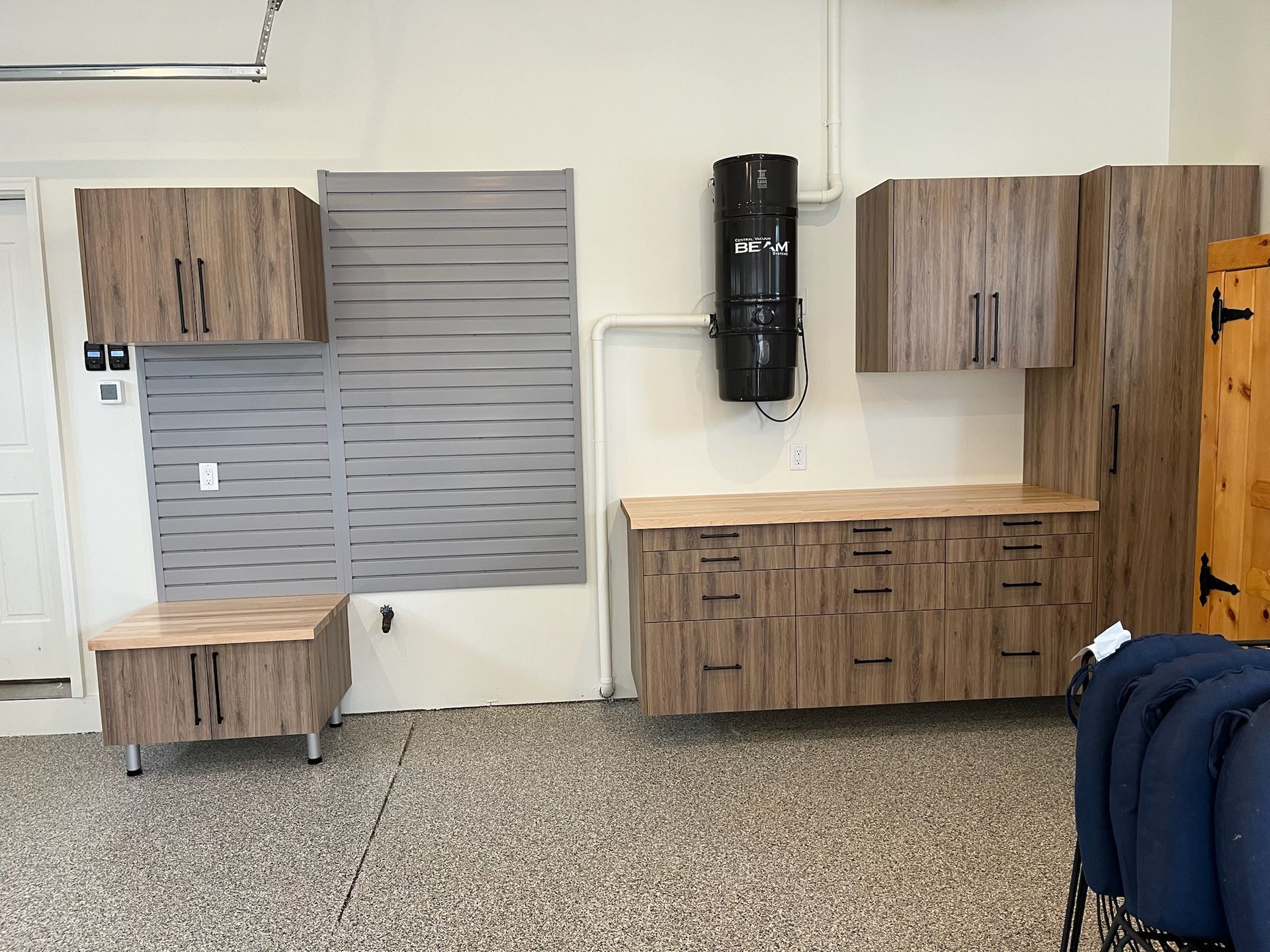 Showroom display of wood cabinets, gray shutter panel, and black wall-mounted dispenser on a white wall