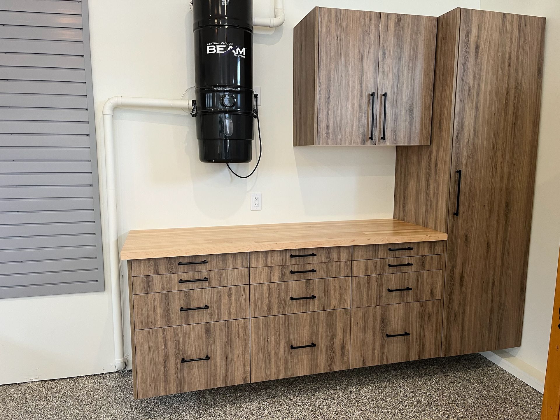 Woodgrain kitchen cabinets with a light wood countertop in a modern room, black tank and gray shutter on wall
