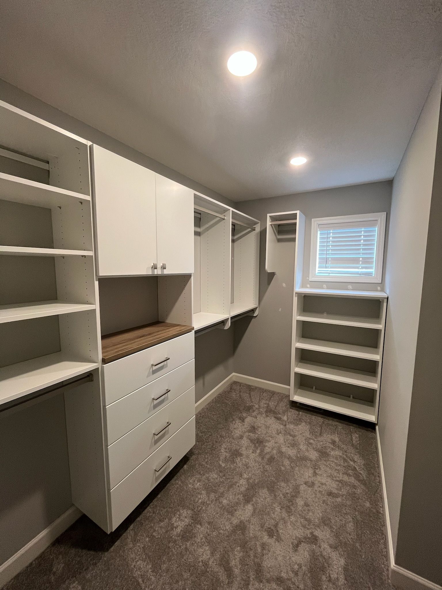 Walk-in closet with white shelving, drawers, hanging rods, and carpeted floor under recessed lights