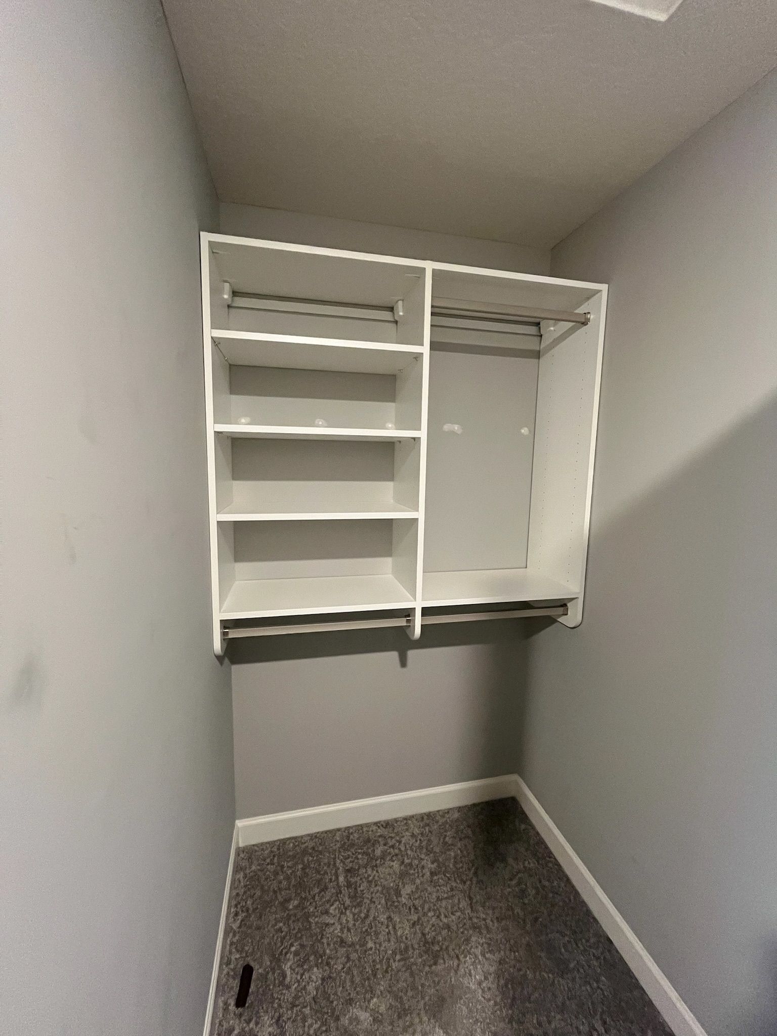 Small walk-in closet with white built-in shelves, hanging rods, and gray carpet.