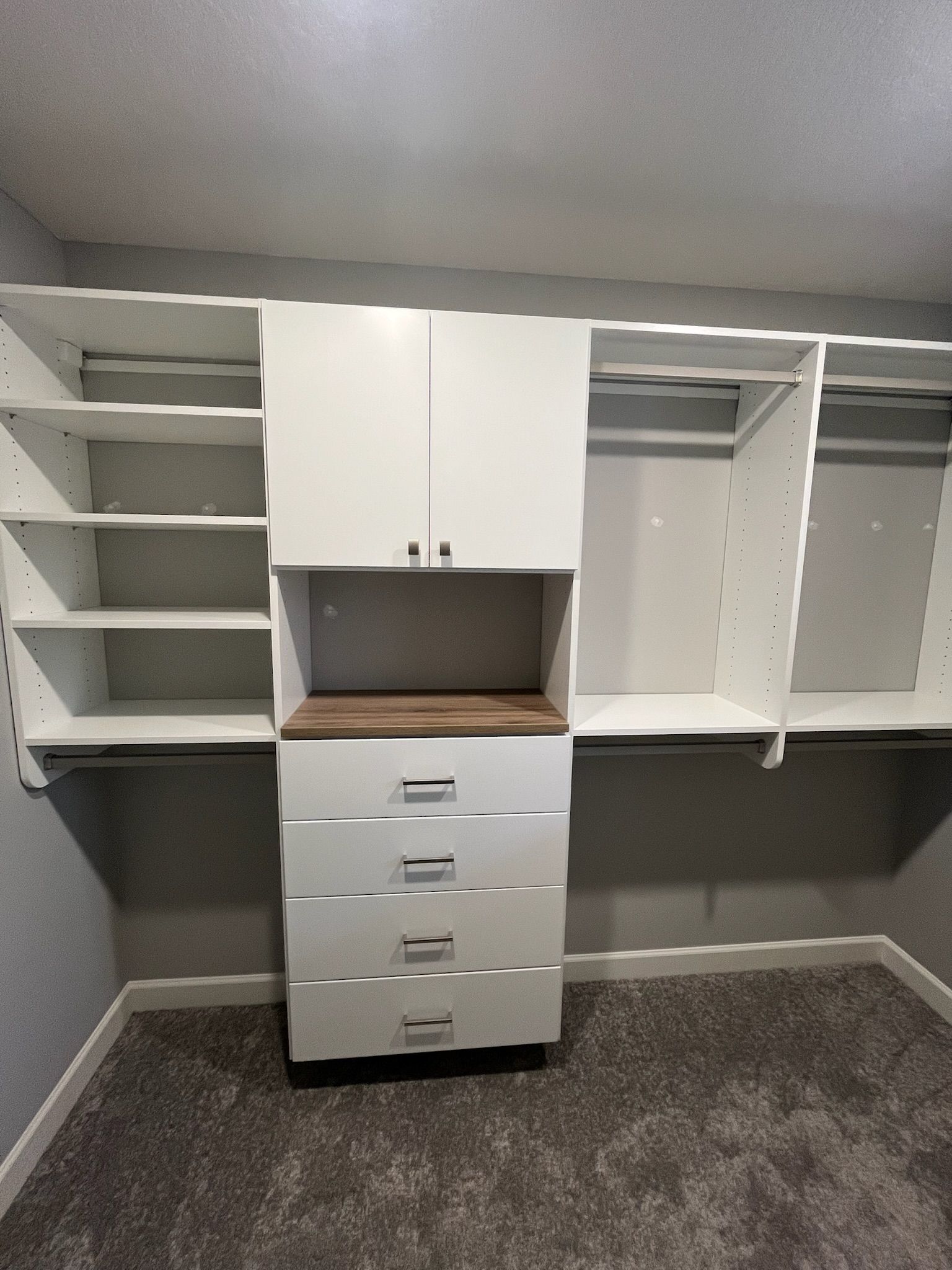 Built-in white closet organizer with shelves, cabinets, drawers, and hanging space against a gray wall.