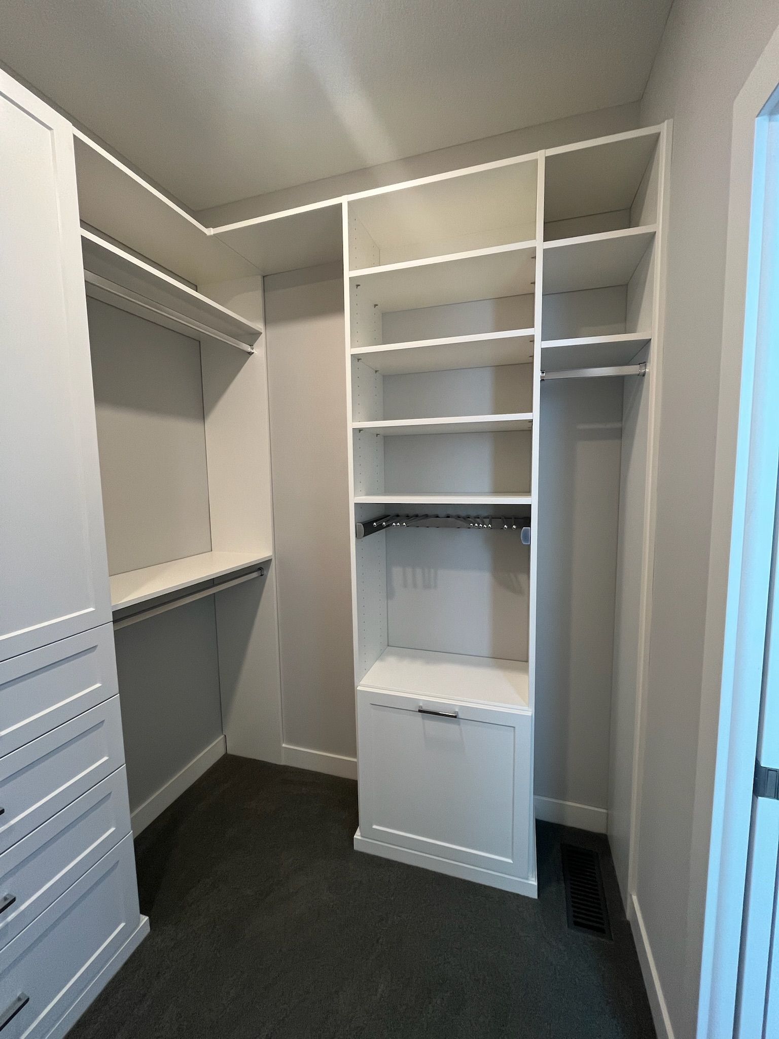Walk-in closet with white shelving and drawers, gray carpet, and an open hanging rod area.
